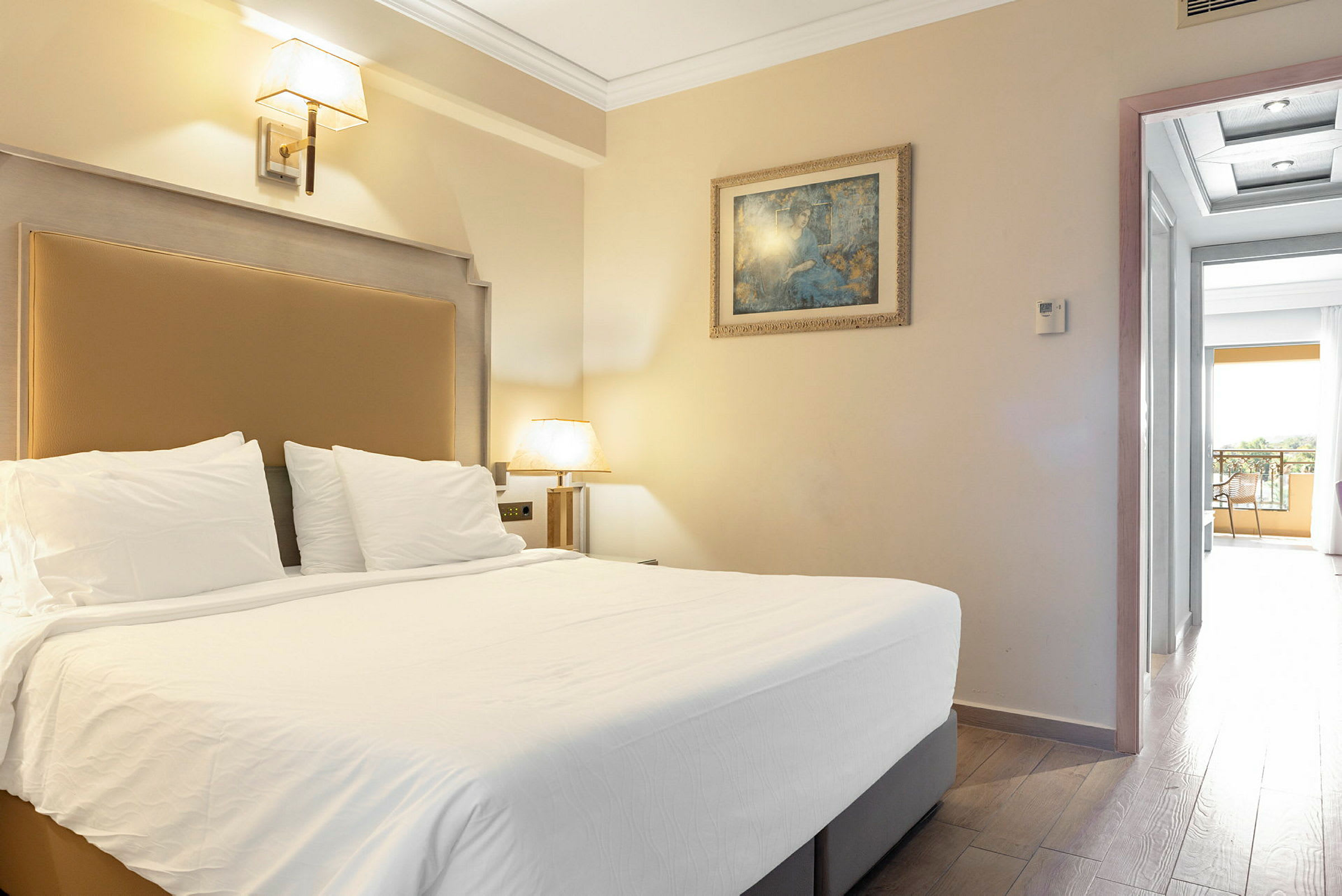 Bild på ett hotellrum med en dubbelsäng, vägglampa, målning och öppning mot en balkong. (AI-genererad text)