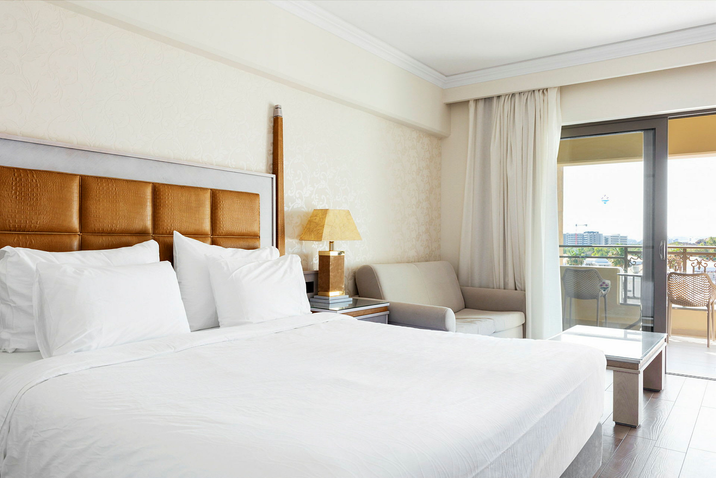 Hotellrum med en stor säng, soffa, och balkong med utsikt utomhus. (AI-genererad text)
