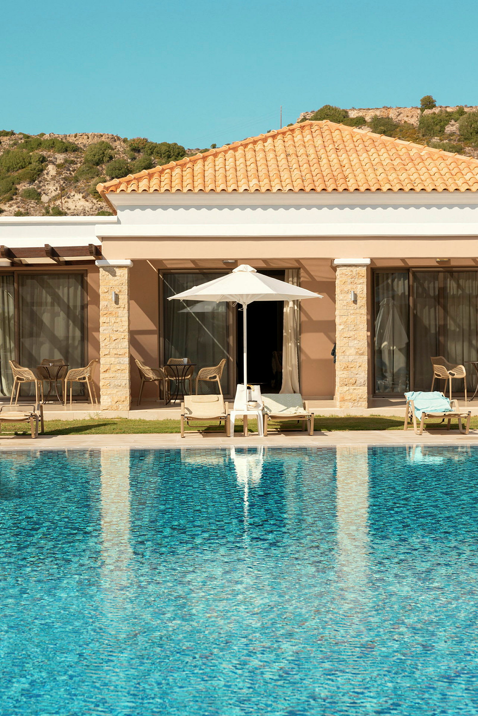 Pool framför hotellbyggnad med solsängar och parasoll. (AI-genererad text)