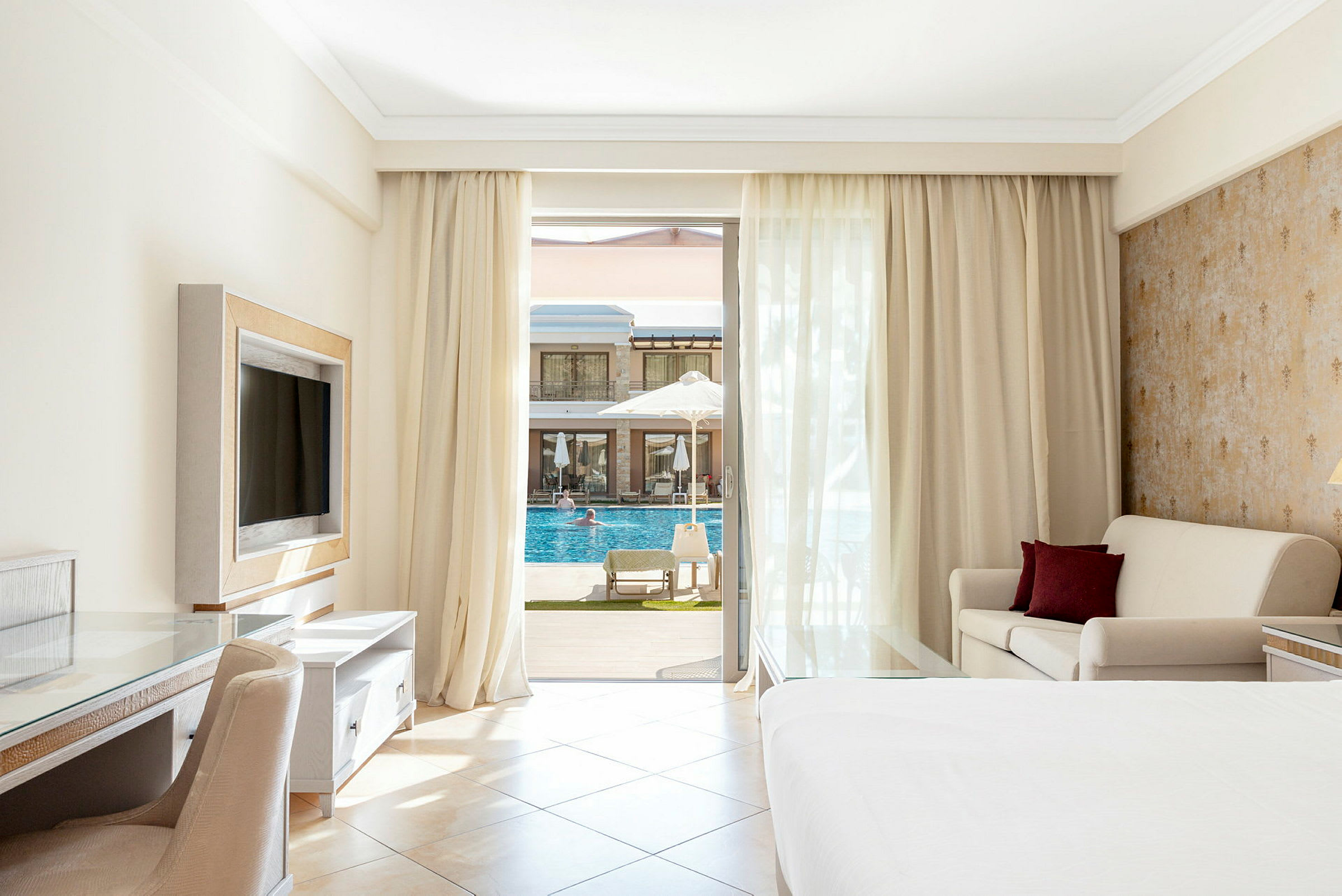 Hotellrum med balkong, säng, soffa och utsikt mot en pool. (AI-genererad text)