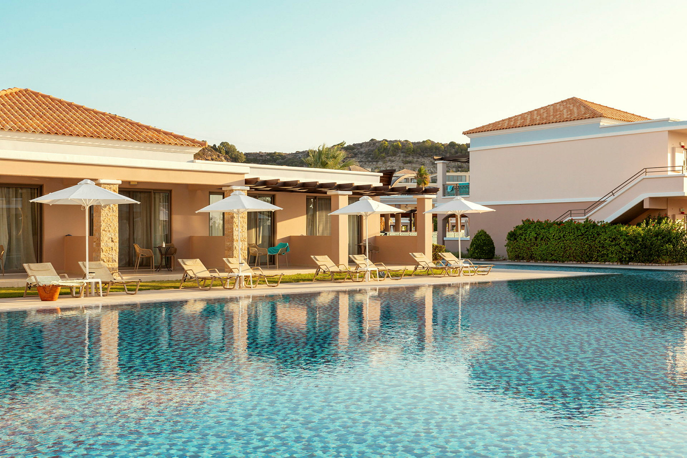 Hotellområde med pool, solstolar och parasoller framför byggnader. (AI-genererad text)