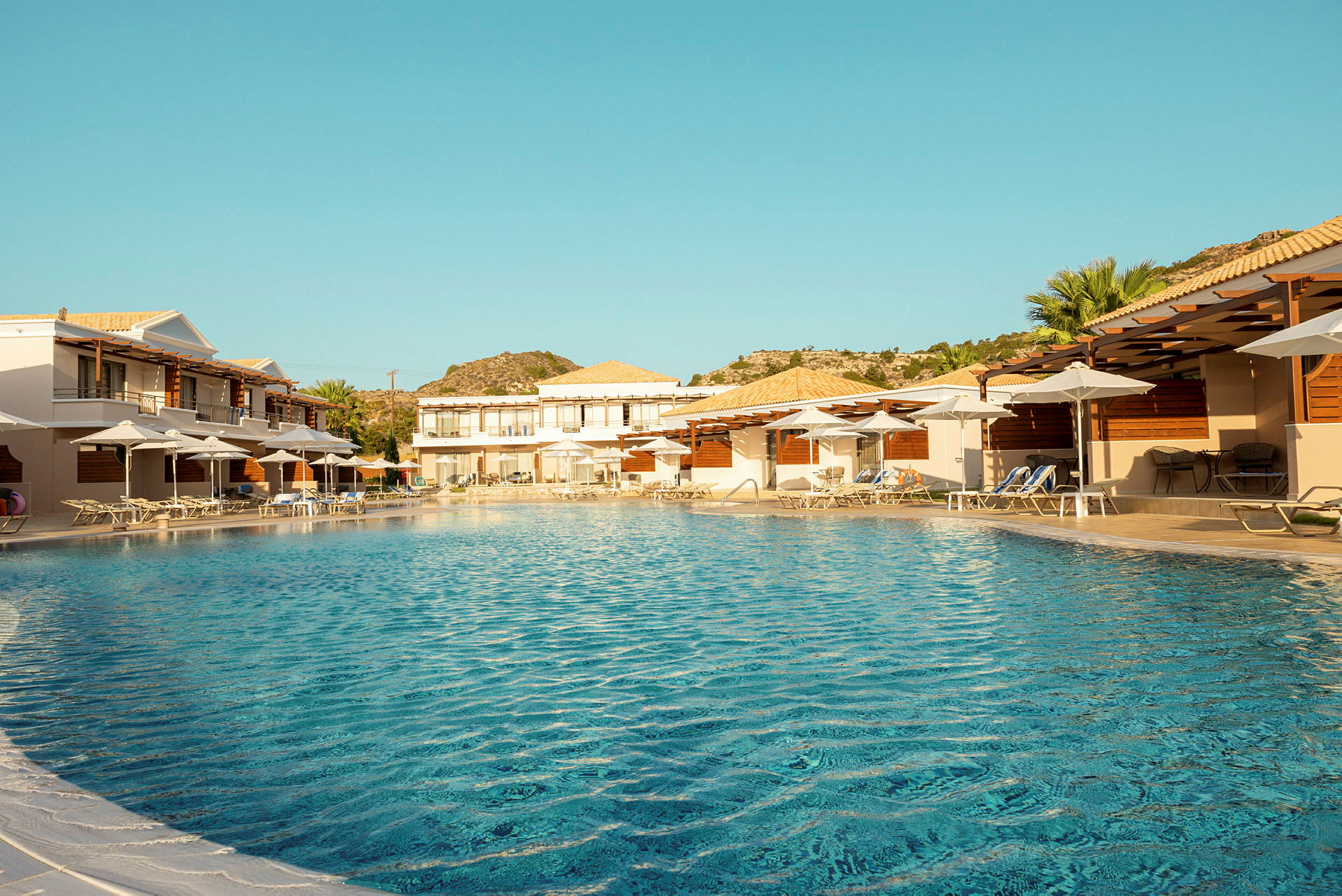Bilden visar en swimmingpool med solstolar och parasoller omgärdade av hotellbyggnader. (AI-genererad text)