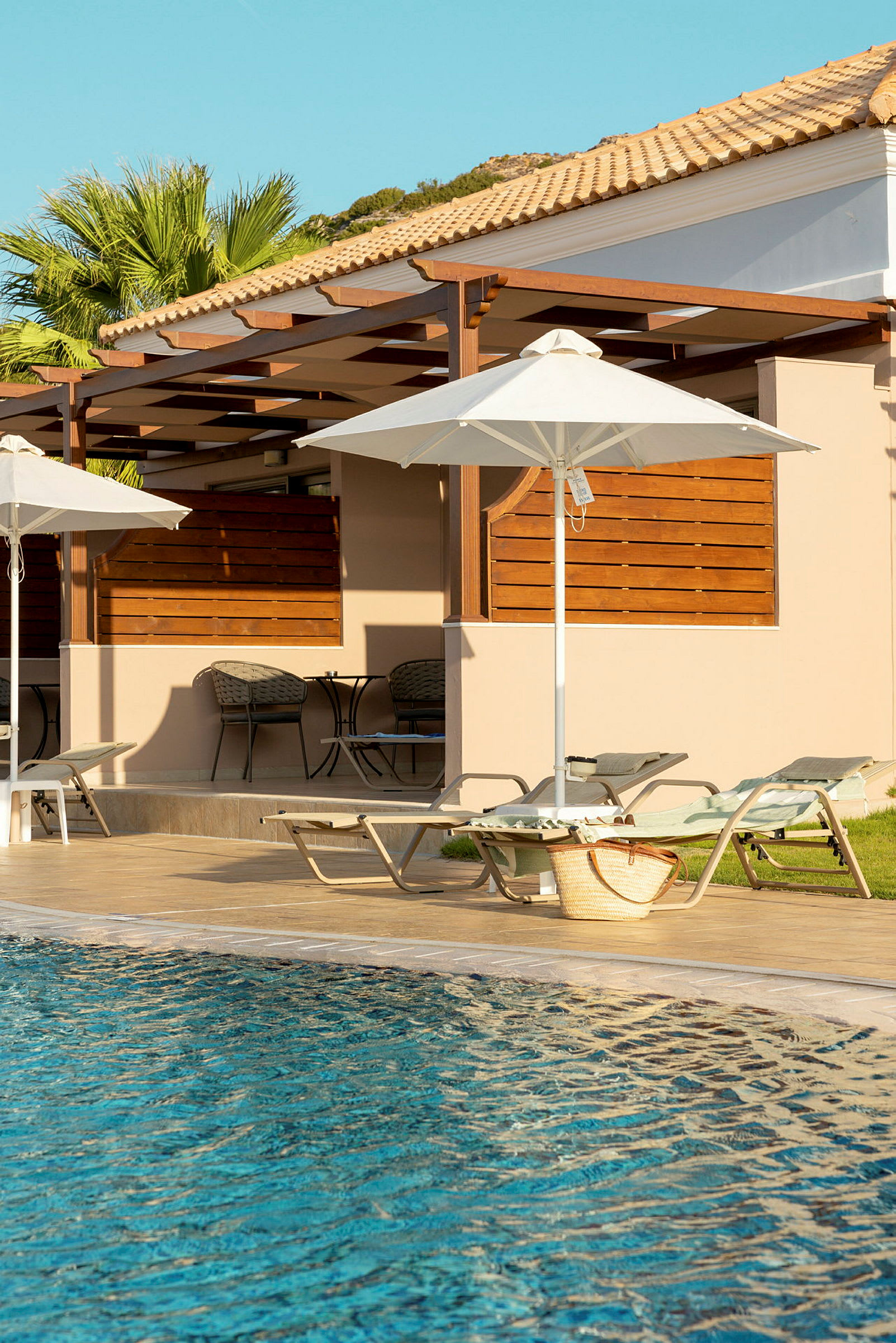 Pool med solsängar under parasoller vid sidan av en byggnad. (AI-genererad text)