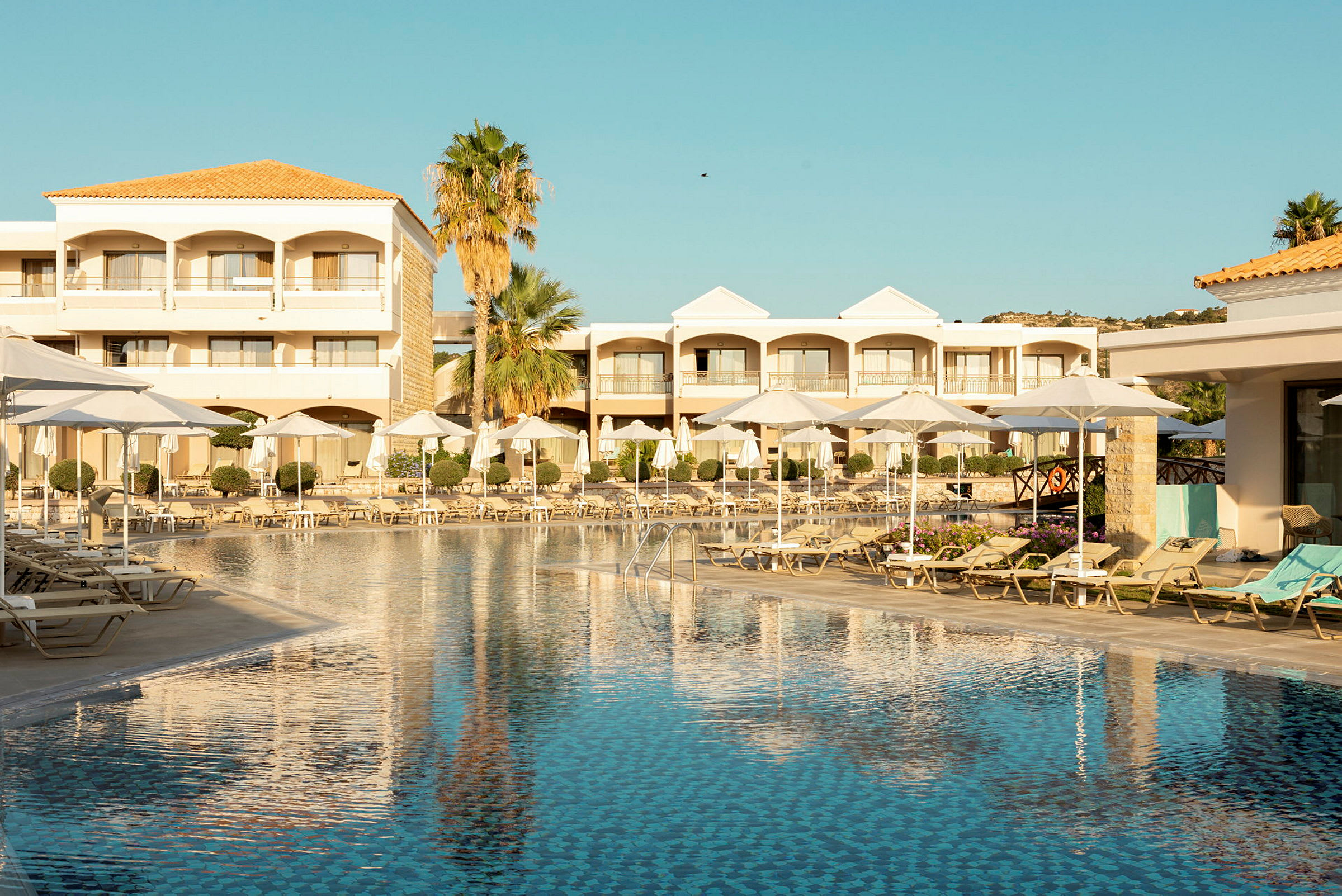 Hotellpool med solstolar och parasoller, omgiven av byggnader och palmer. (AI-genererad text)