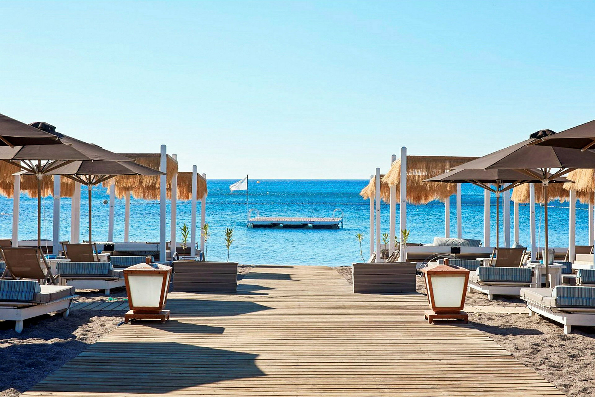 Strand med solstolar och parasoller, brygga i havet. (AI-genererad text)