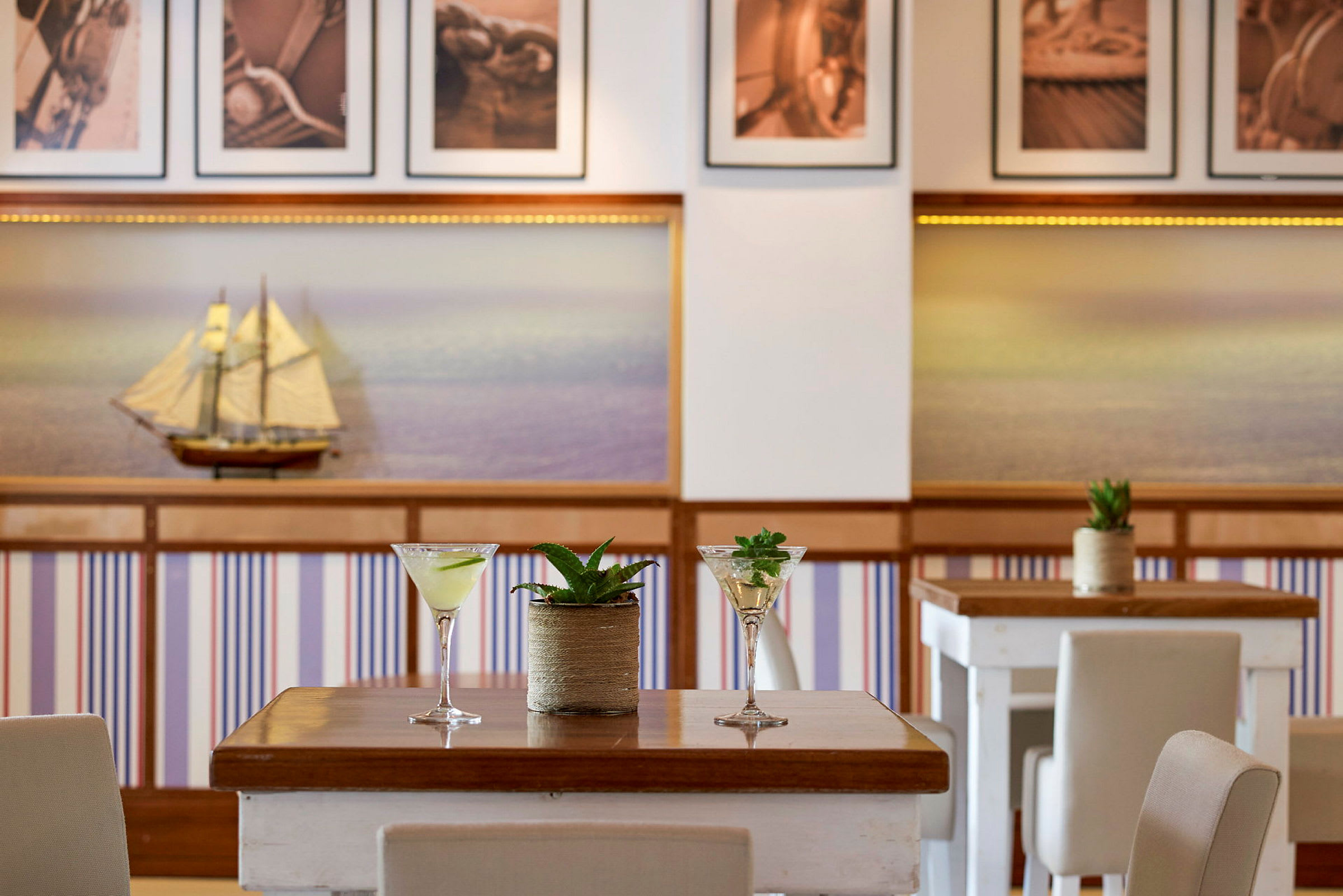 Bord med cocktailglas och växter, inredningen visar en modell av segelbåt och panoramabilder. (AI-genererad text)