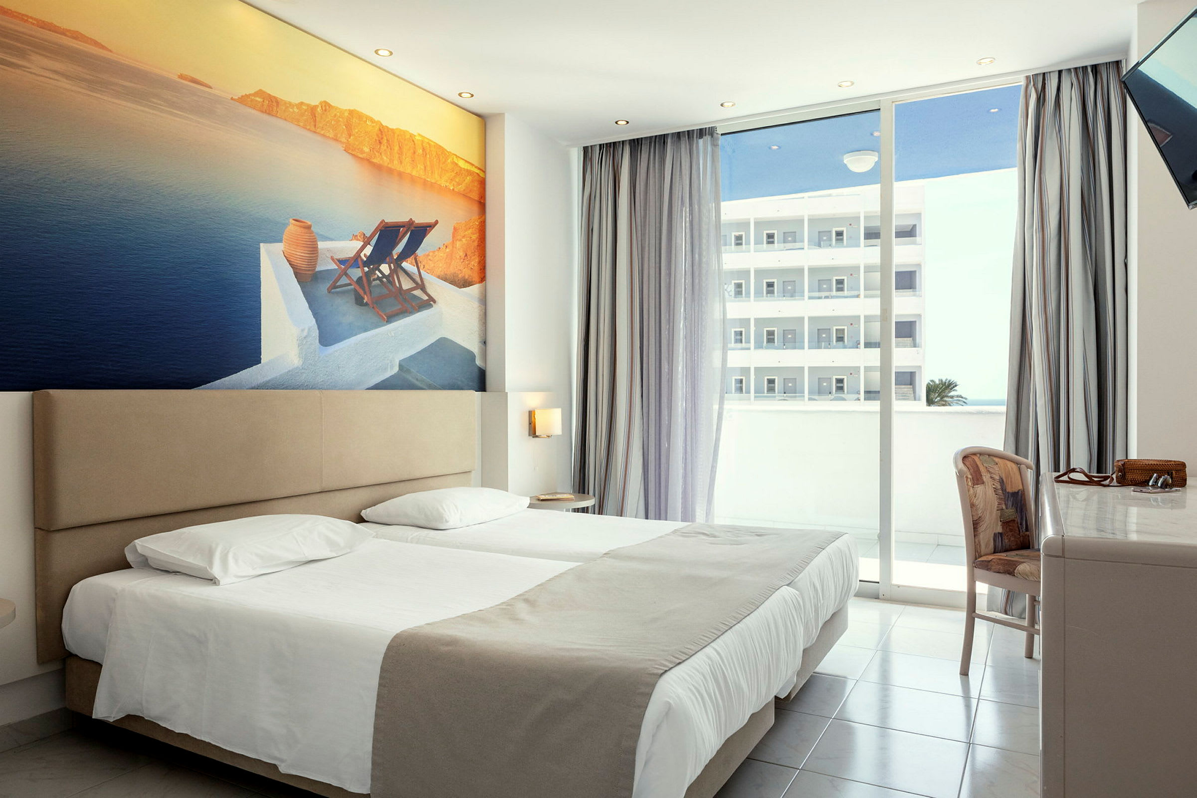 Hotellrum med dubbelsäng, stor väggbild av ett kustlandskap och balkong med utsikt. (AI-genererad text)
