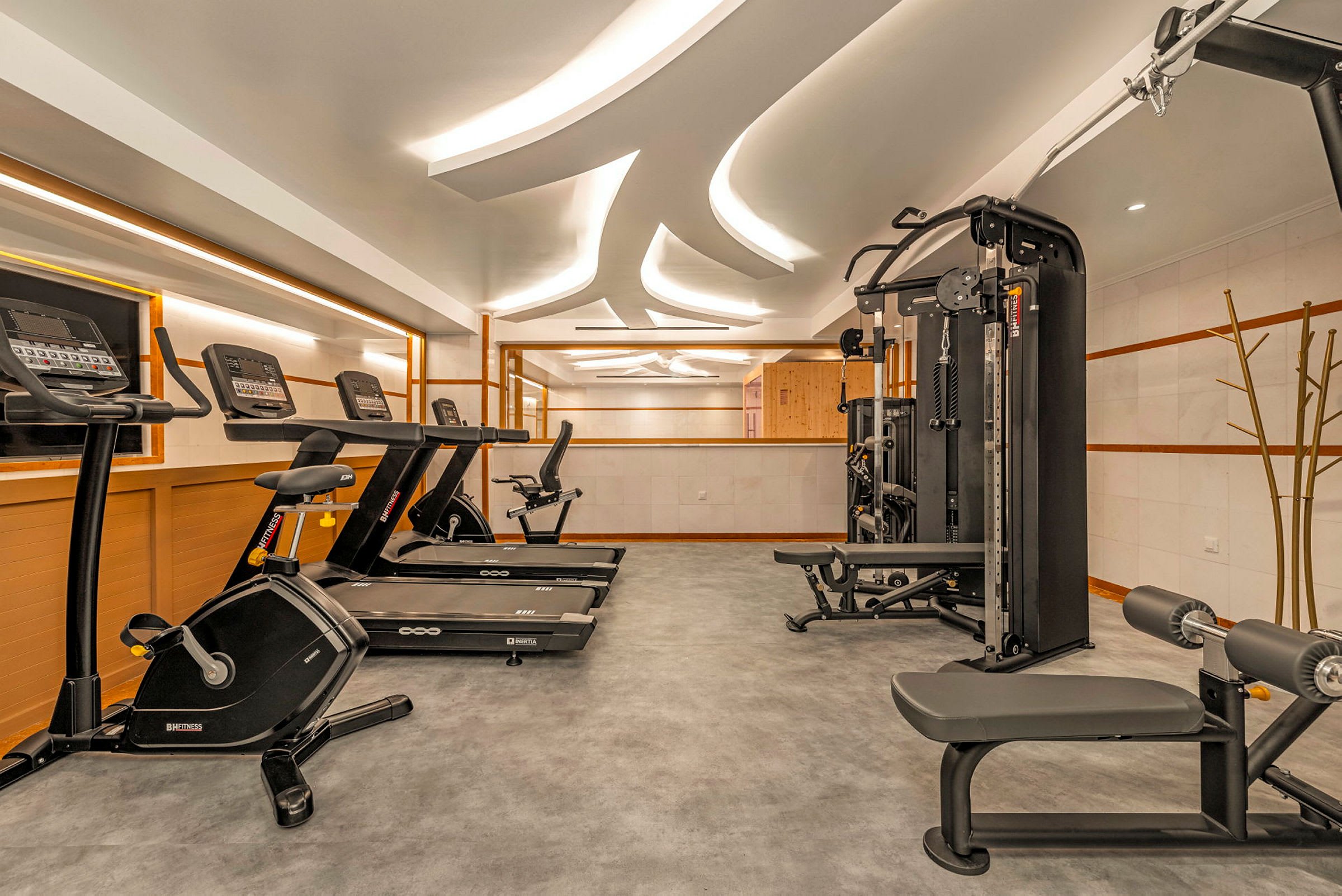 Ett modernt gym med olika träningsmaskiner som löpband, motionscykel och multigym. Takbelysning och spegelväggar skapar en ljus och rymlig miljö. (AI-genererad text)