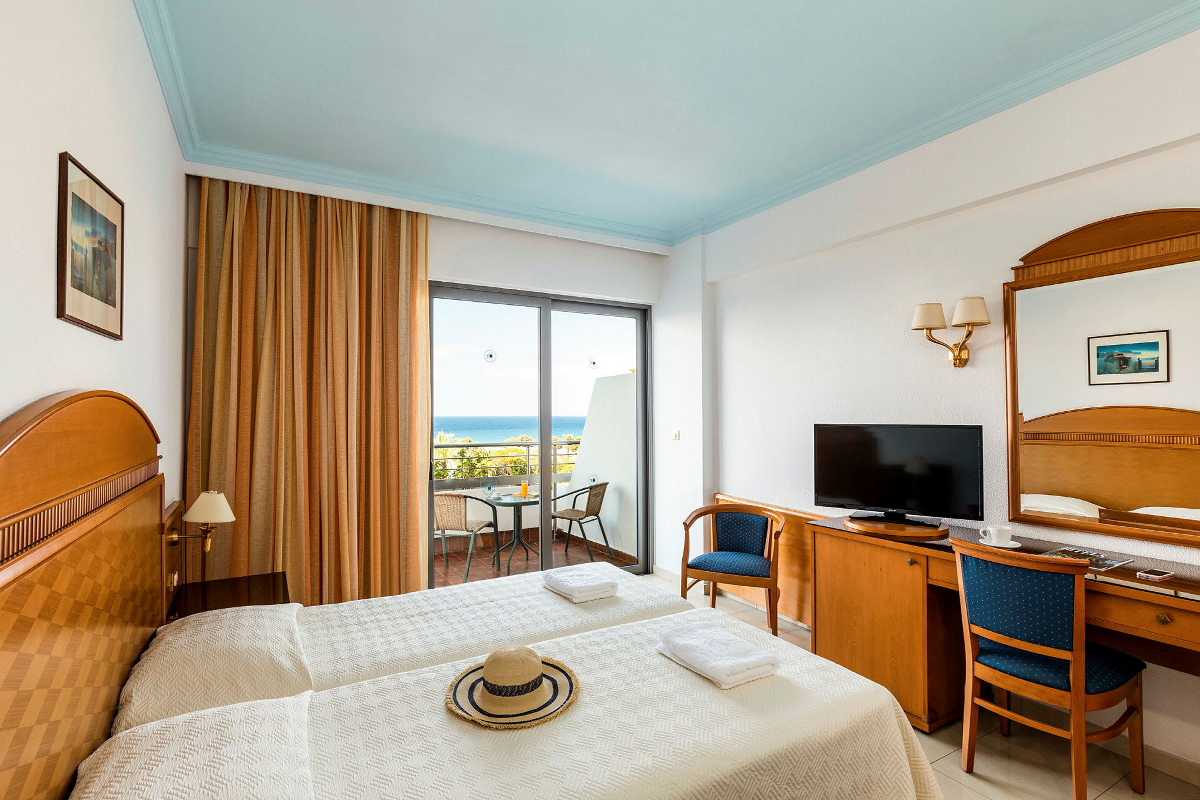 Hotellrum med två enkelsängar, ett träskrivbord med stol och en balkong med utsikt över havet. (AI-genererad text)