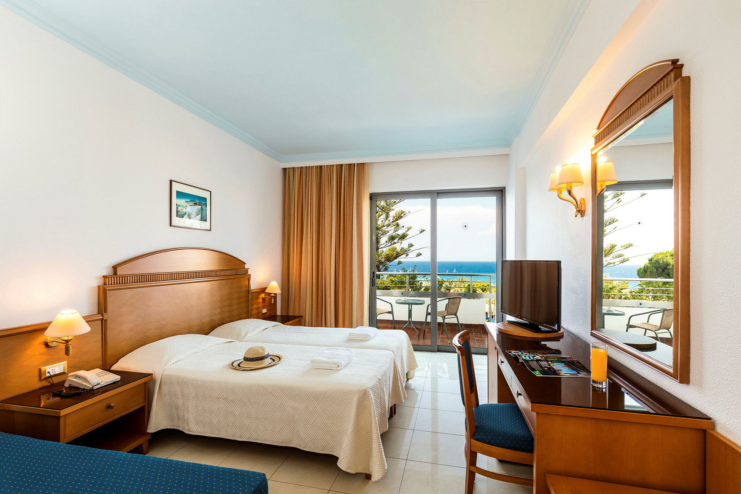 Ett hotellrum med två sängar, ett skrivbord, en spegel och en balkong med utsikt över havet. (AI-genererad text)