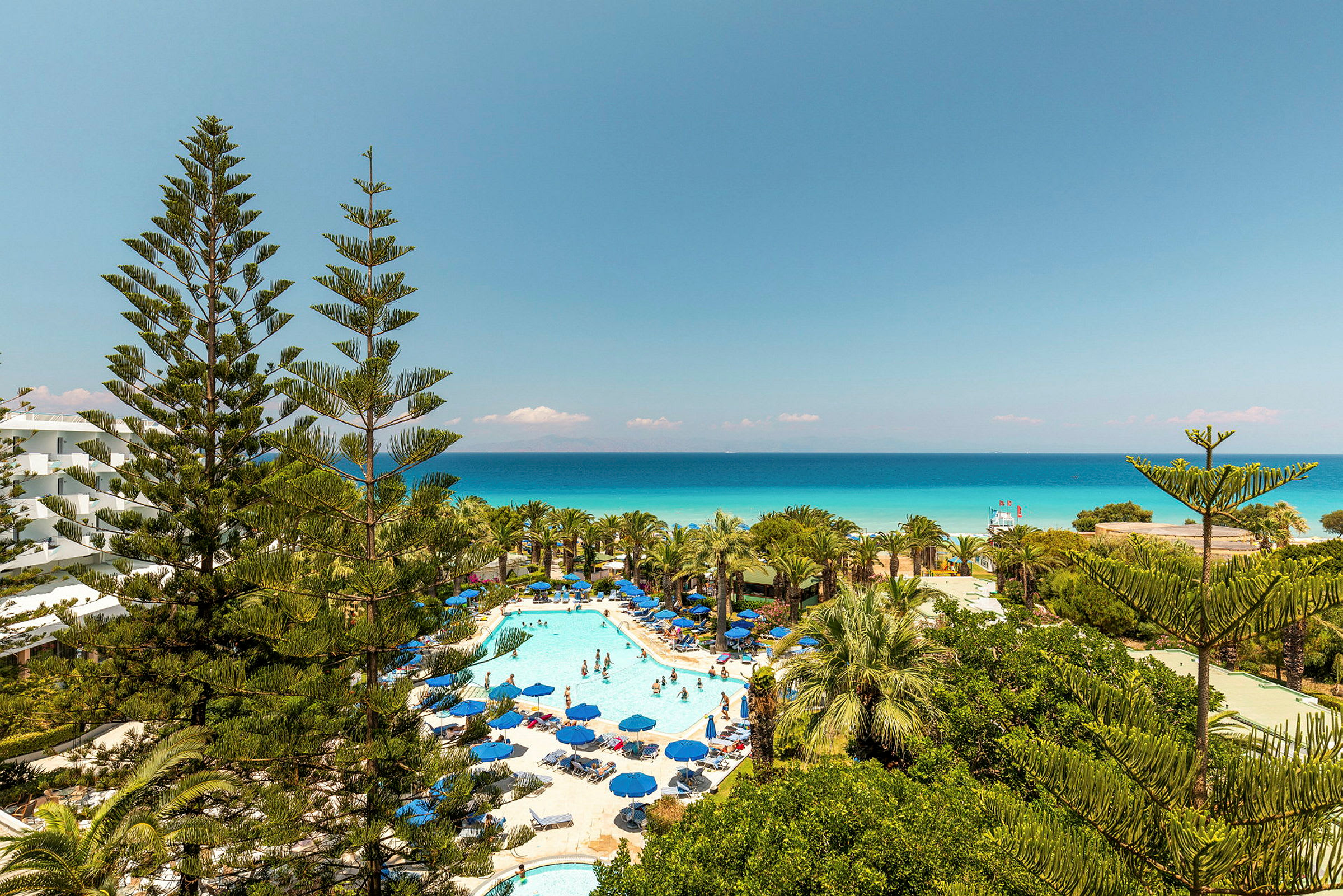 Bild av hotellområde med pool och solsängar omgivna av grönska och utsikt mot havet. (AI-genererad text)