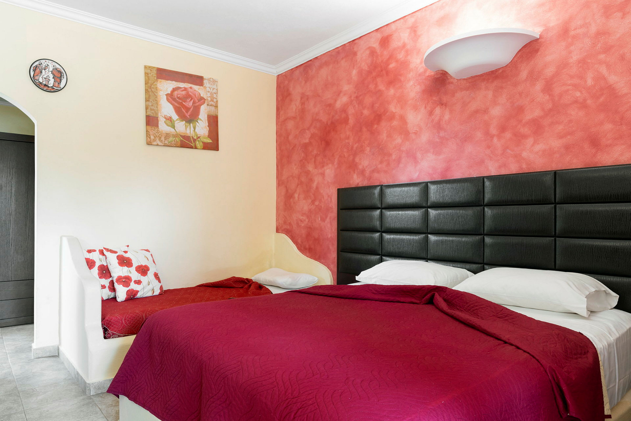 Ett hotellrum med en säng klädd i röda sängkläder och en målning på väggen. (AI-genererad text)