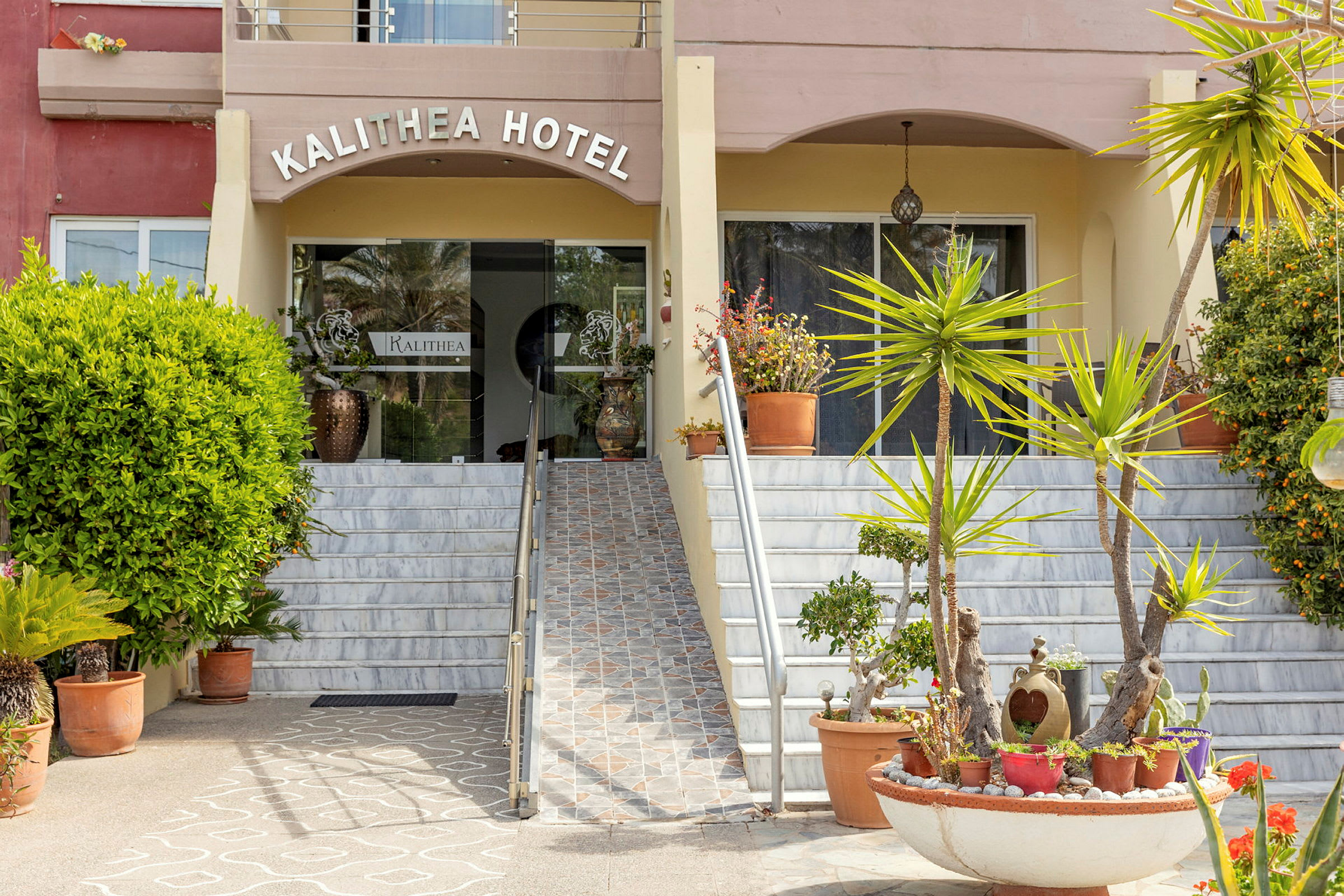Entrén till Kalithea Hotel med trappor och planteringar i förgrunden. (AI-genererad text)