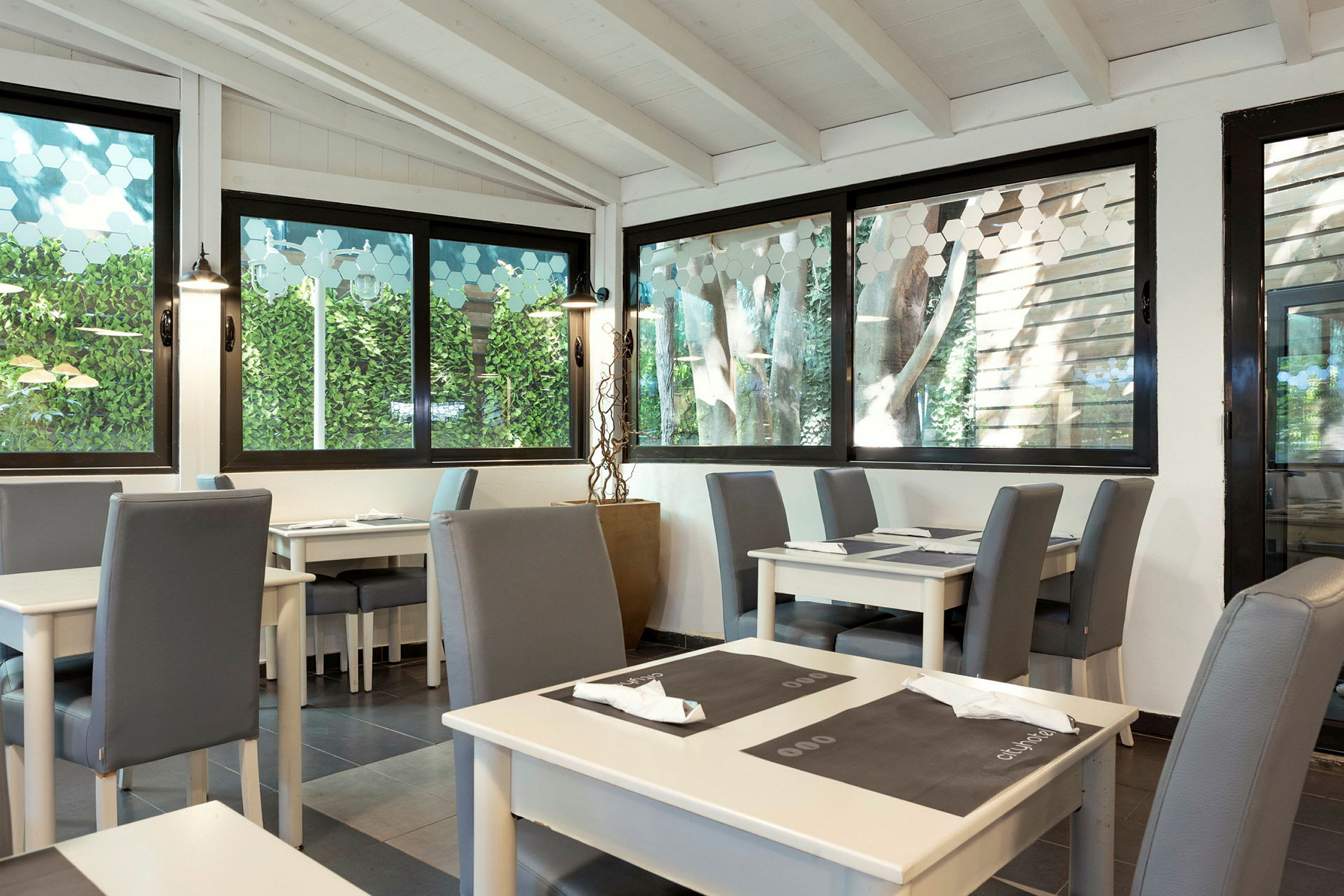 Ett ljust restauranginteriör med glasfönster och sittplatser. (AI-genererad text)