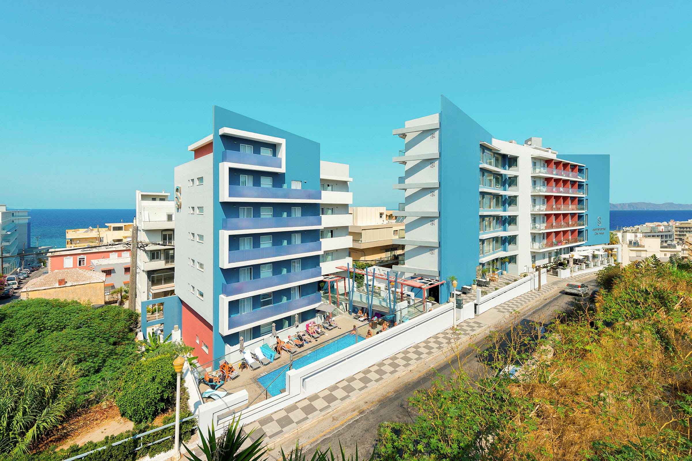 Bild av två moderna hotellbyggnader med blå fasader, en pool och solstolar i förgrunden. (AI-genererad text)