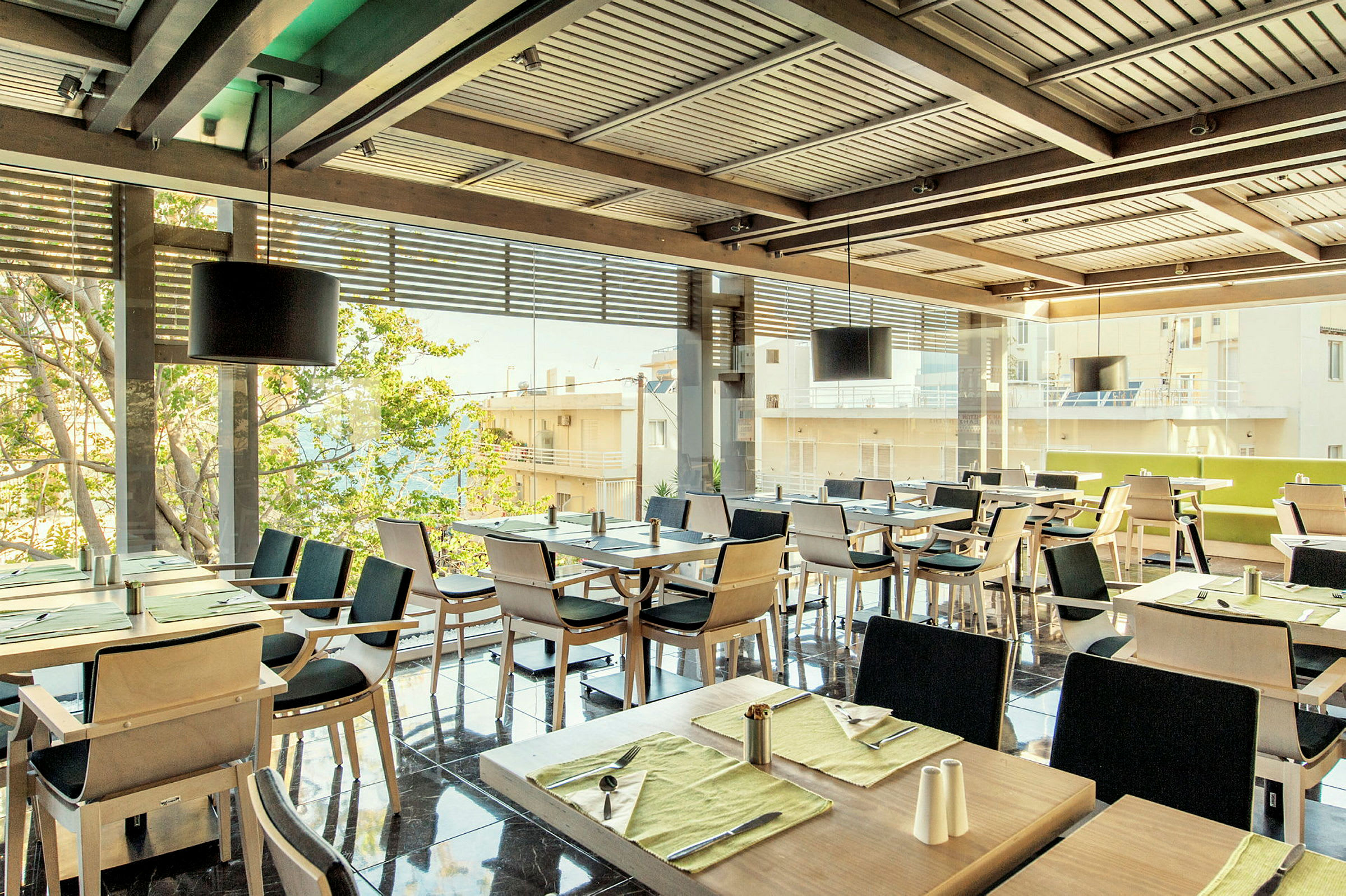 En restaurang med flera dukade bord och stolar, med fönster mot en stadsvy. (AI-genererad text)