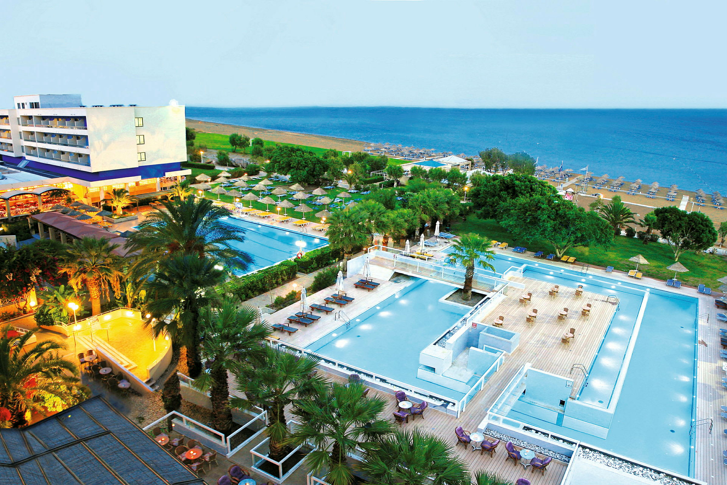 Utsikt över ett hotellområde med swimmingpooler och grönska, och i bakgrunden syns en sandstrand och havet. (AI-genererad text)