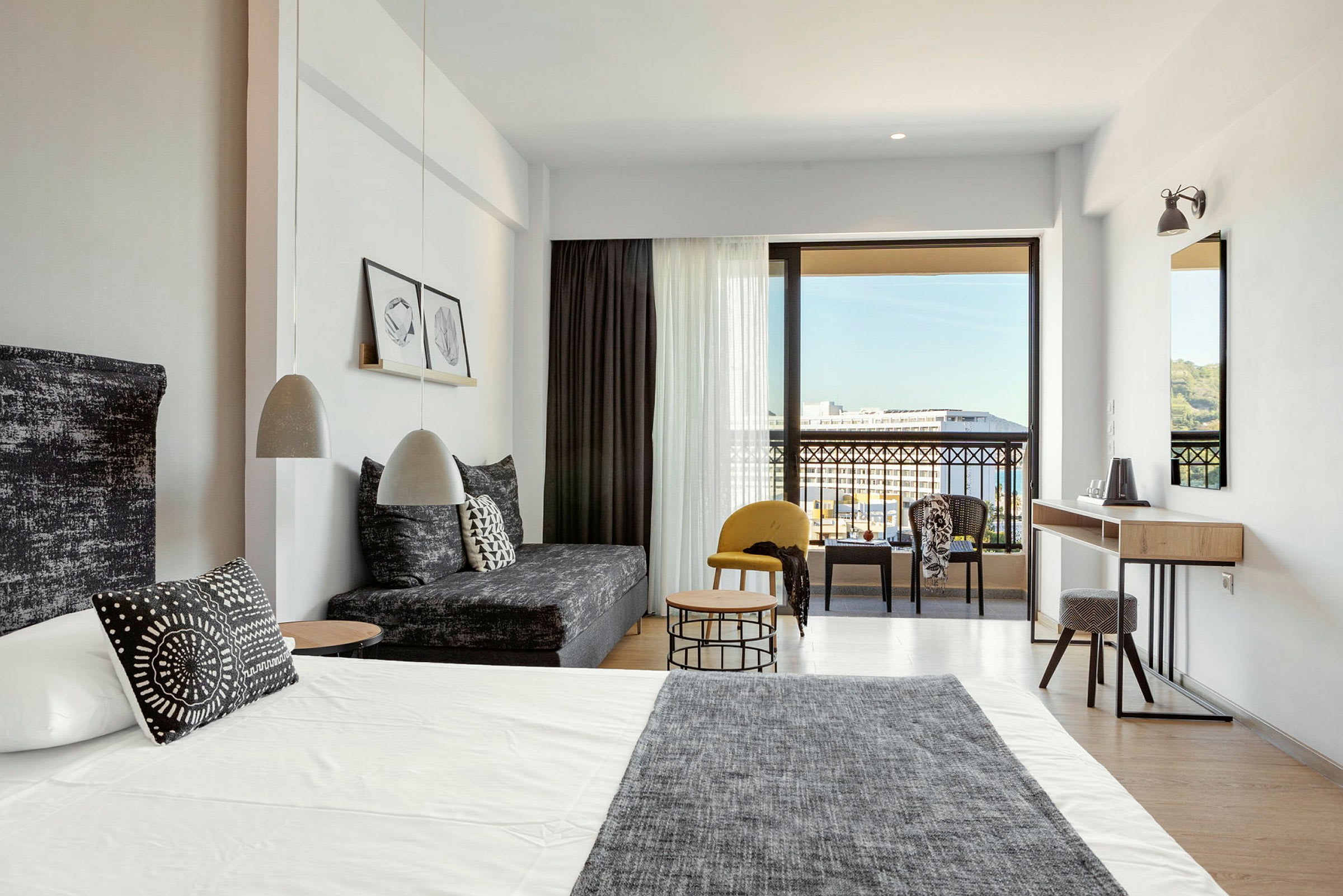Modernt hotellrum med säng, soffa och sittgrupp samt utsikt mot balkong och omgivning. (AI-genererad text)