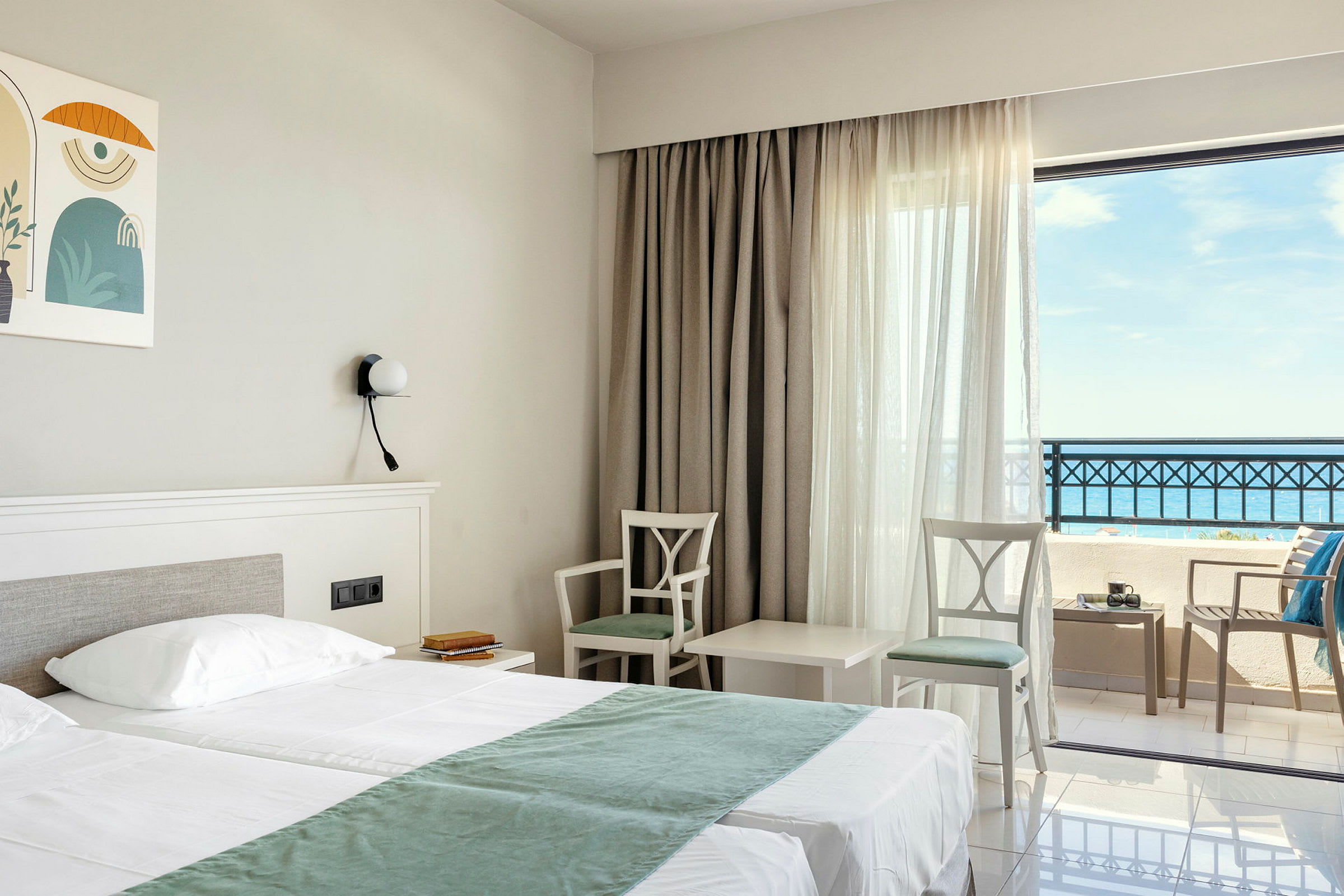 Hotellrum med dubbelsäng, två stolar och ett bord vid fönster med havsutsikt. (AI-genererad text)