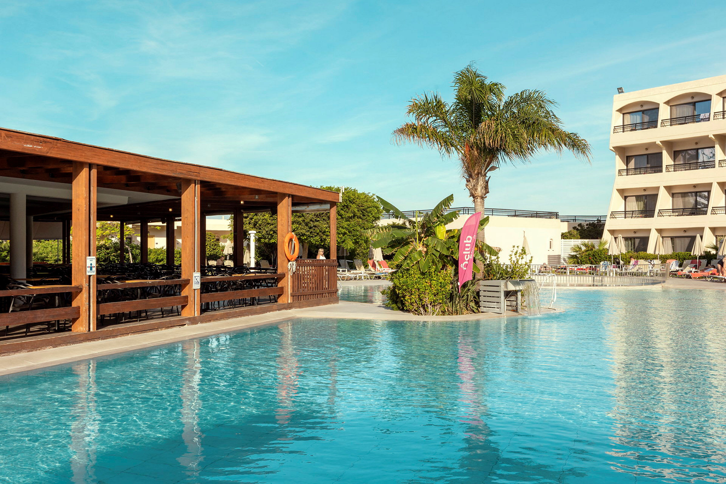 Bild av en pool, en terrass med sittmöbler, en palm och hotellbyggnader. (AI-genererad text)