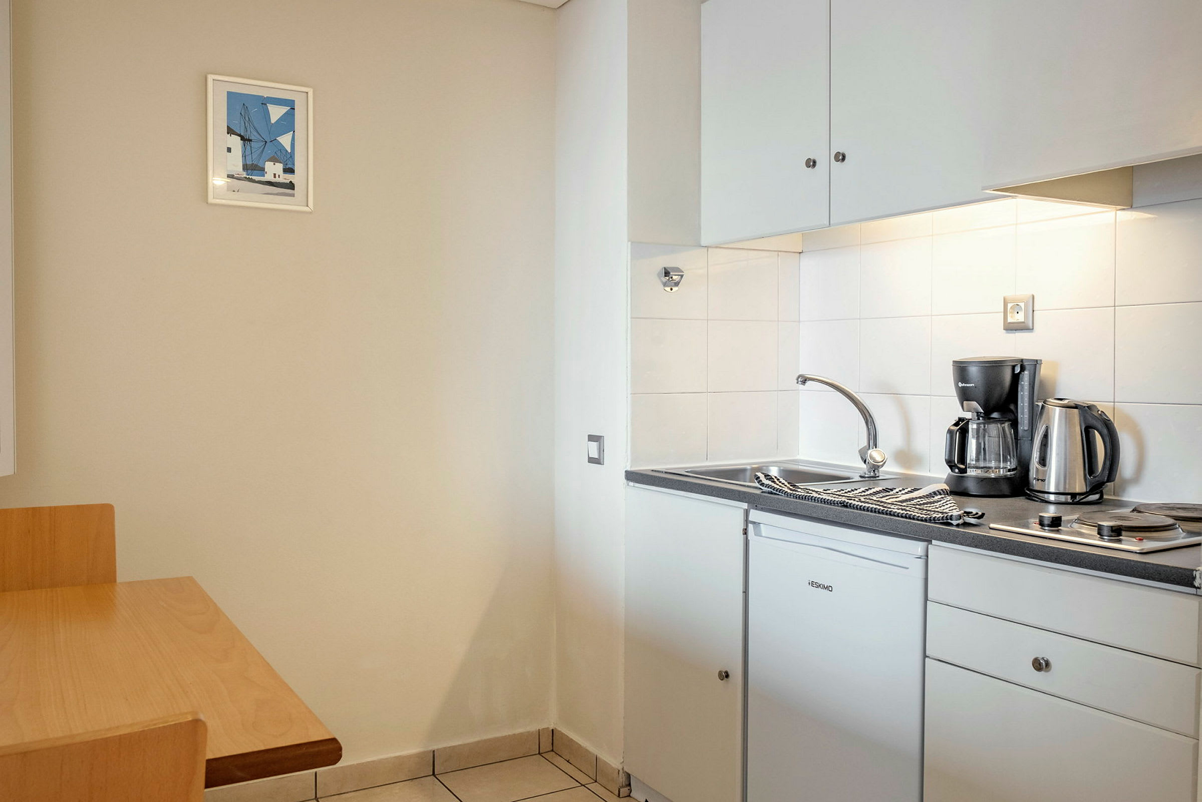 Ett kök med en diskbänk, en kaffemaskin, en vattenkokare och en kokplatta. (AI-genererad text)