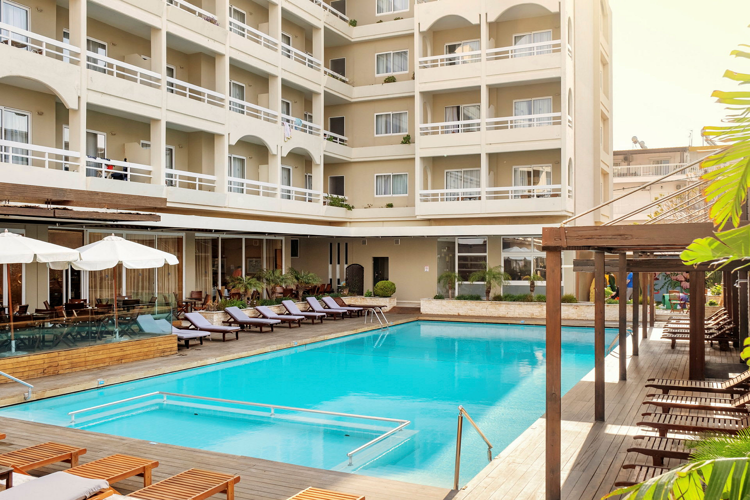 Hotellbyggnad med balkonger och solstolar vid en utomhuspool. (AI-genererad text)