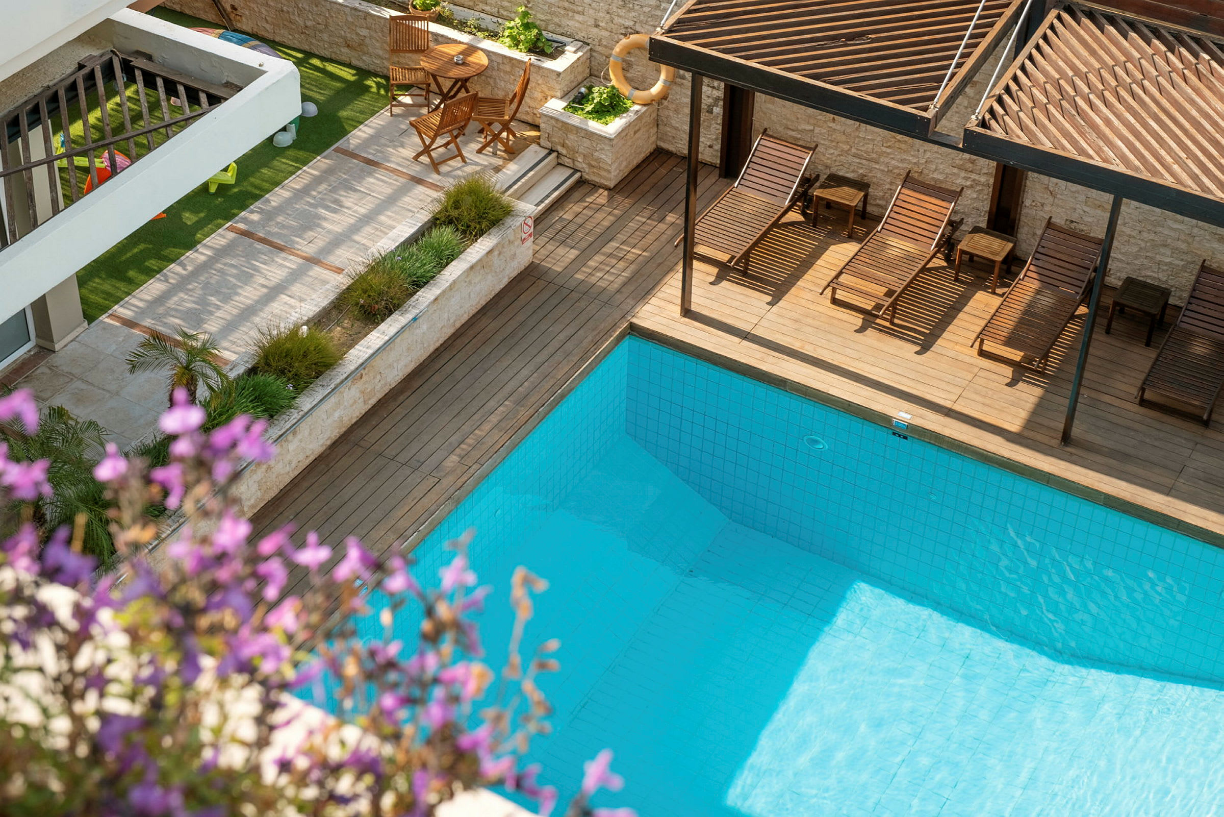 Outdoor swimmingpool med omgivande trädgård och solstolar. Blommor i förgrunden. (AI-genererad text)