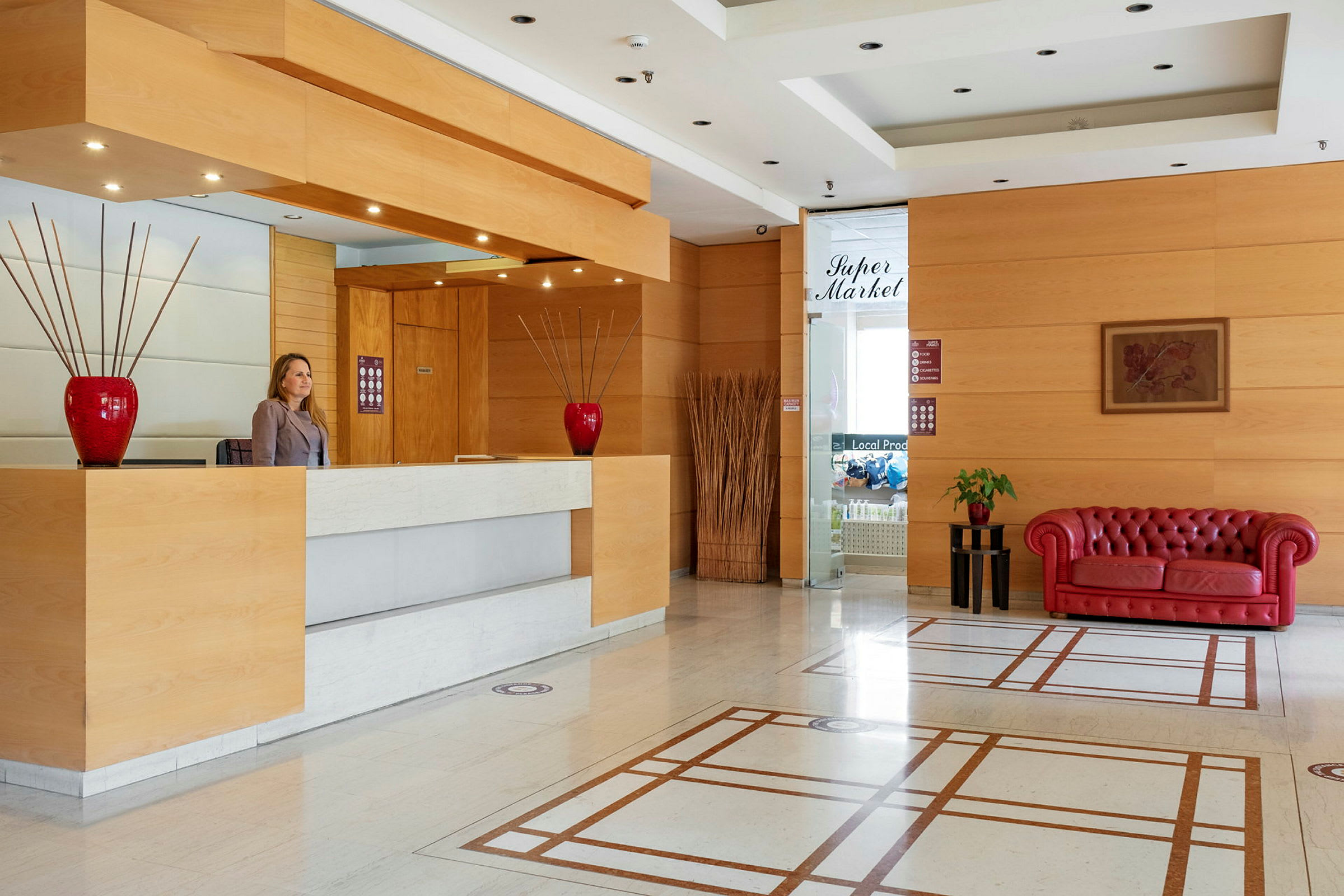 Lobbyn har en reception med en träpanel och röda dekorationer samt en röd soffa. (AI-genererad text)