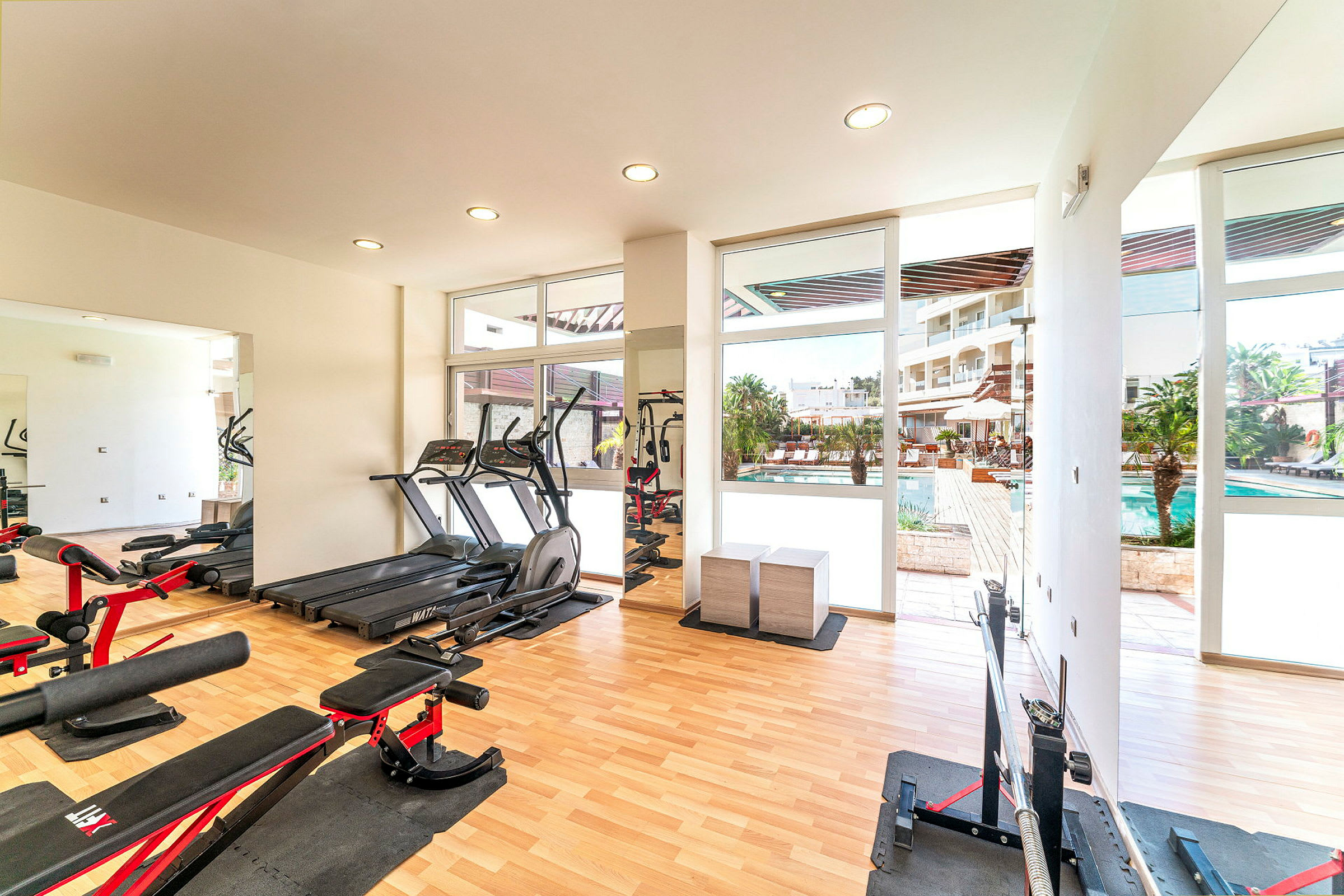 Ett gym med träningsutrustning och fönster som visar en utomhuspool. (AI-genererad text)