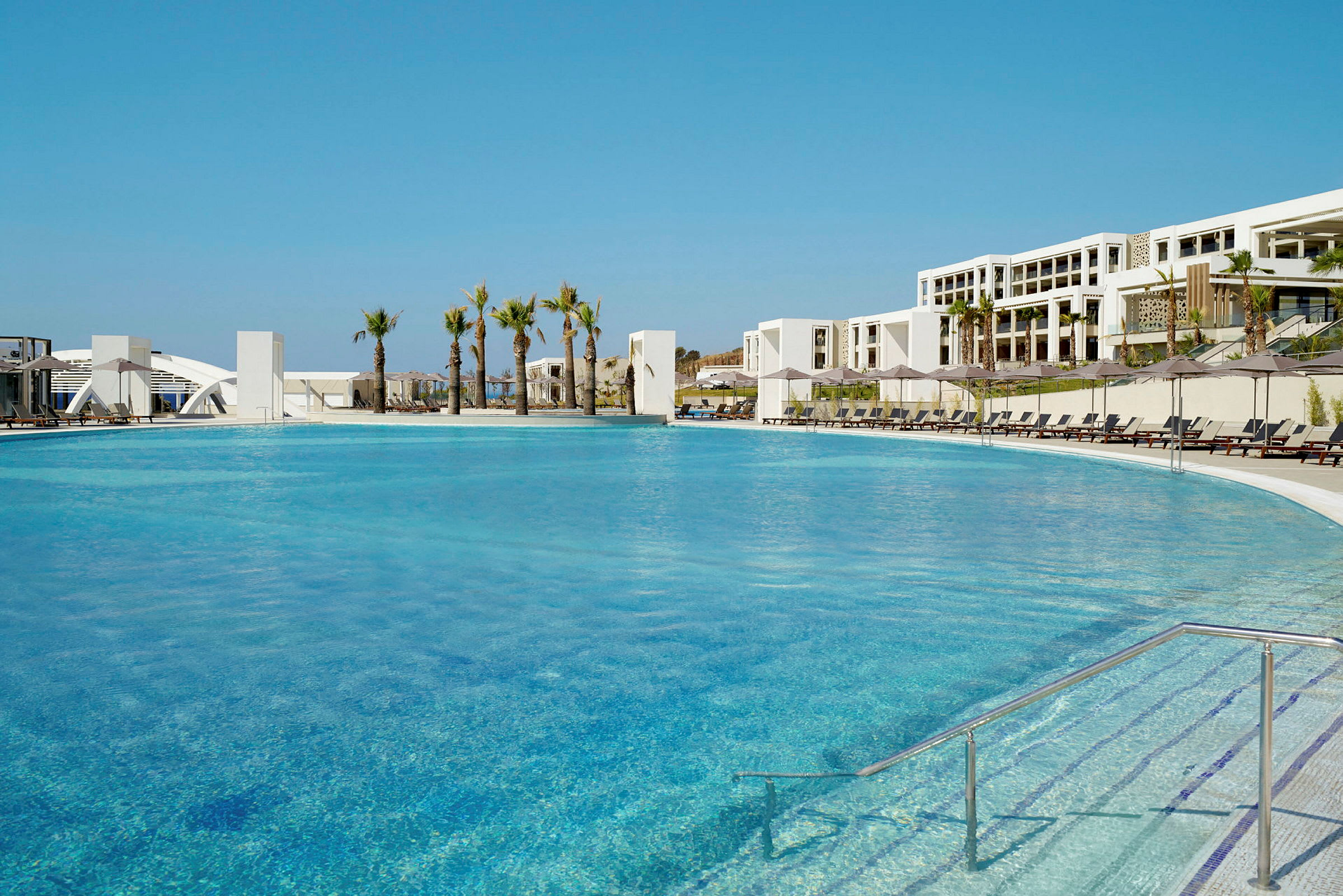 Stor pool omgiven av solstolar och palmer vid ett hotell. (AI-genererad text)