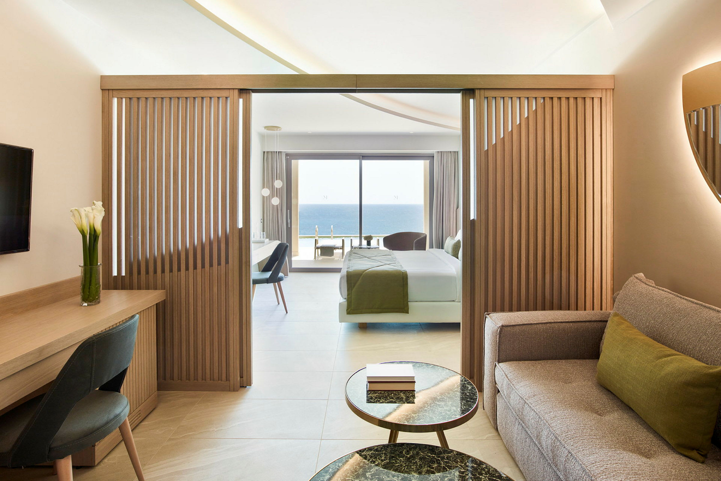 Ett hotellrum med en sittgrupp, arbetsbord, och sovrum som har utsikt över havet. (AI-genererad text)