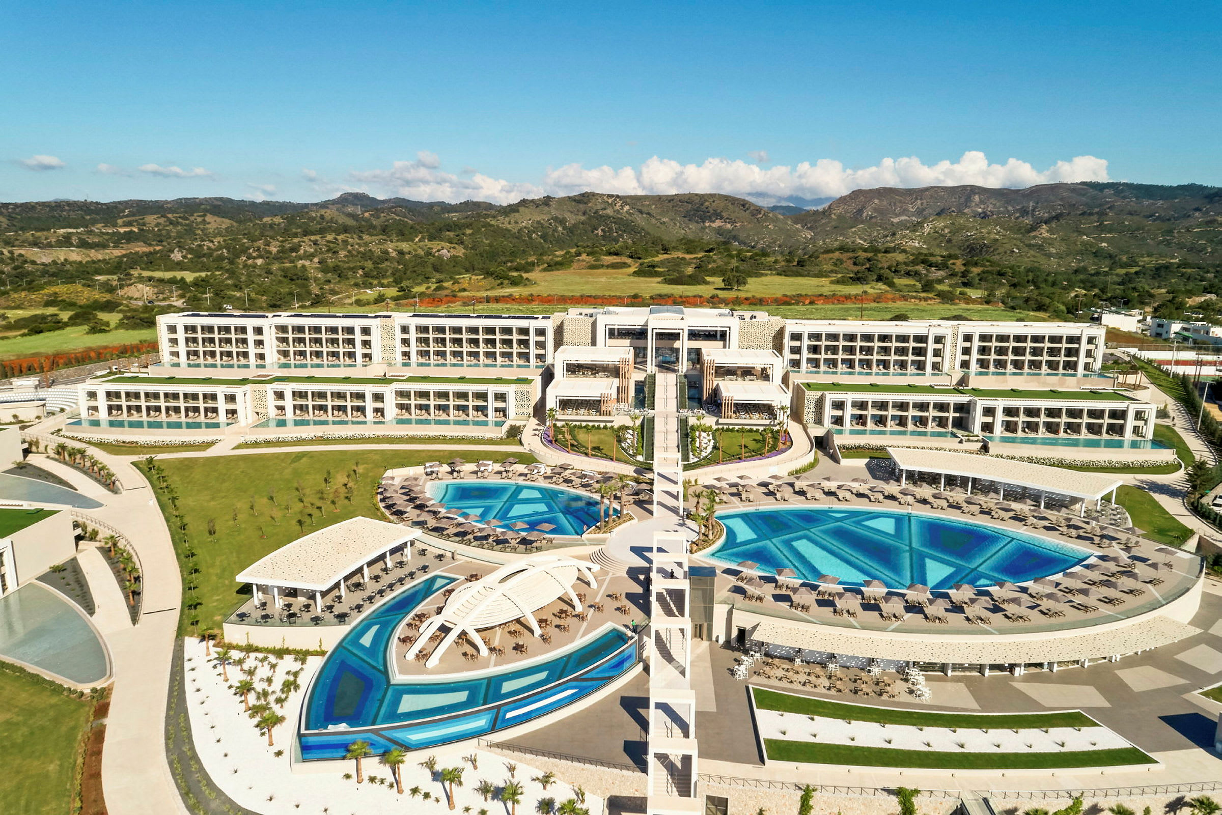 En bild av ett hotellkomplex med flera byggnader, pooler och grönområden, omgivet av landskap. (AI-genererad text)