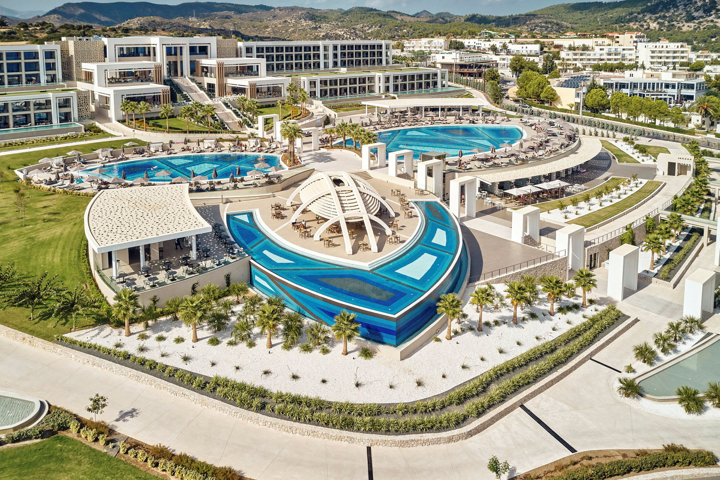 Hotellanläggning med swimmingpooler och moderna byggnader i ett grönt omgivande landskap. (AI-genererad text)