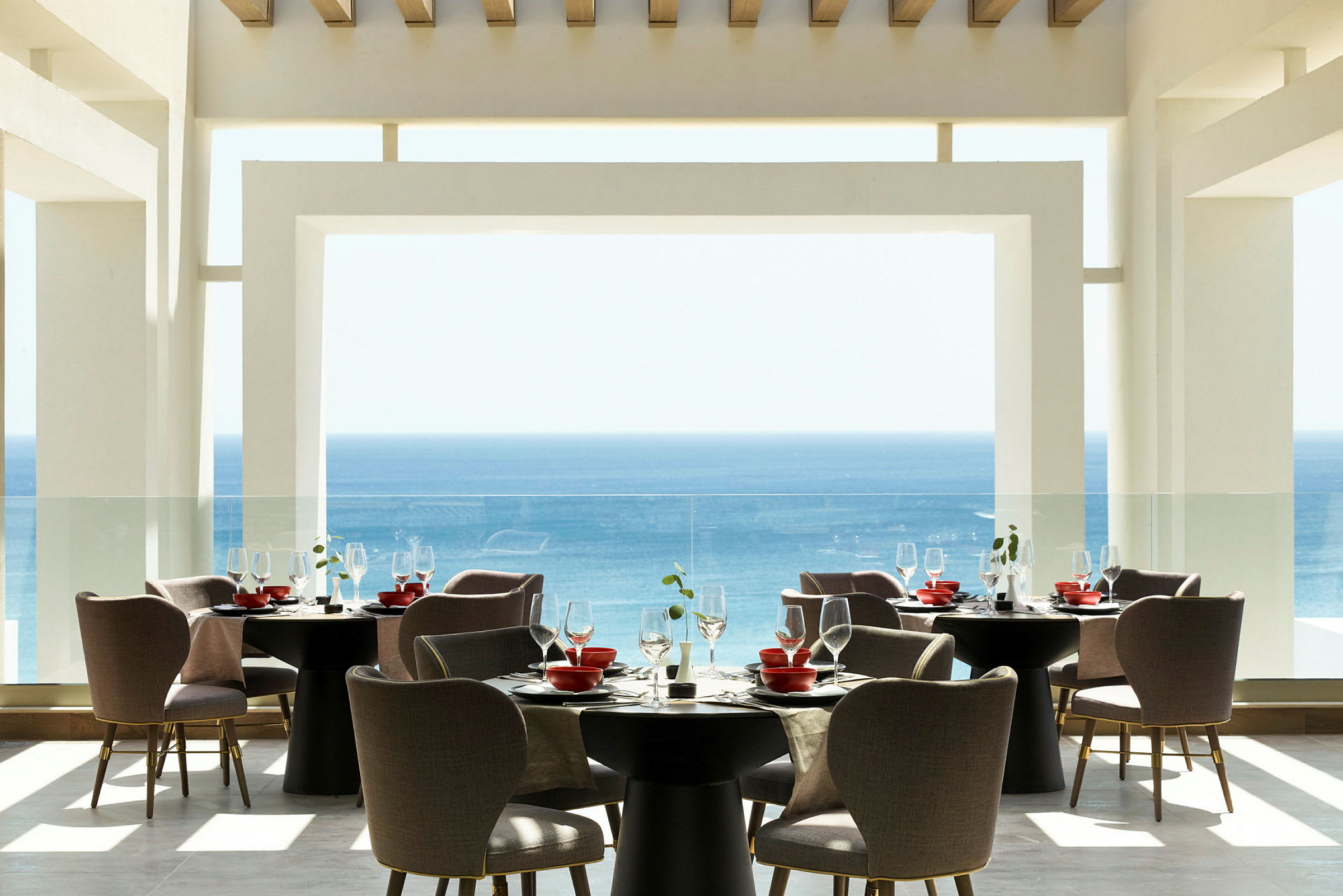 En modern restaurang med utsikt över havet, möblerade med runda bord och bekväma stolar. (AI-genererad text)