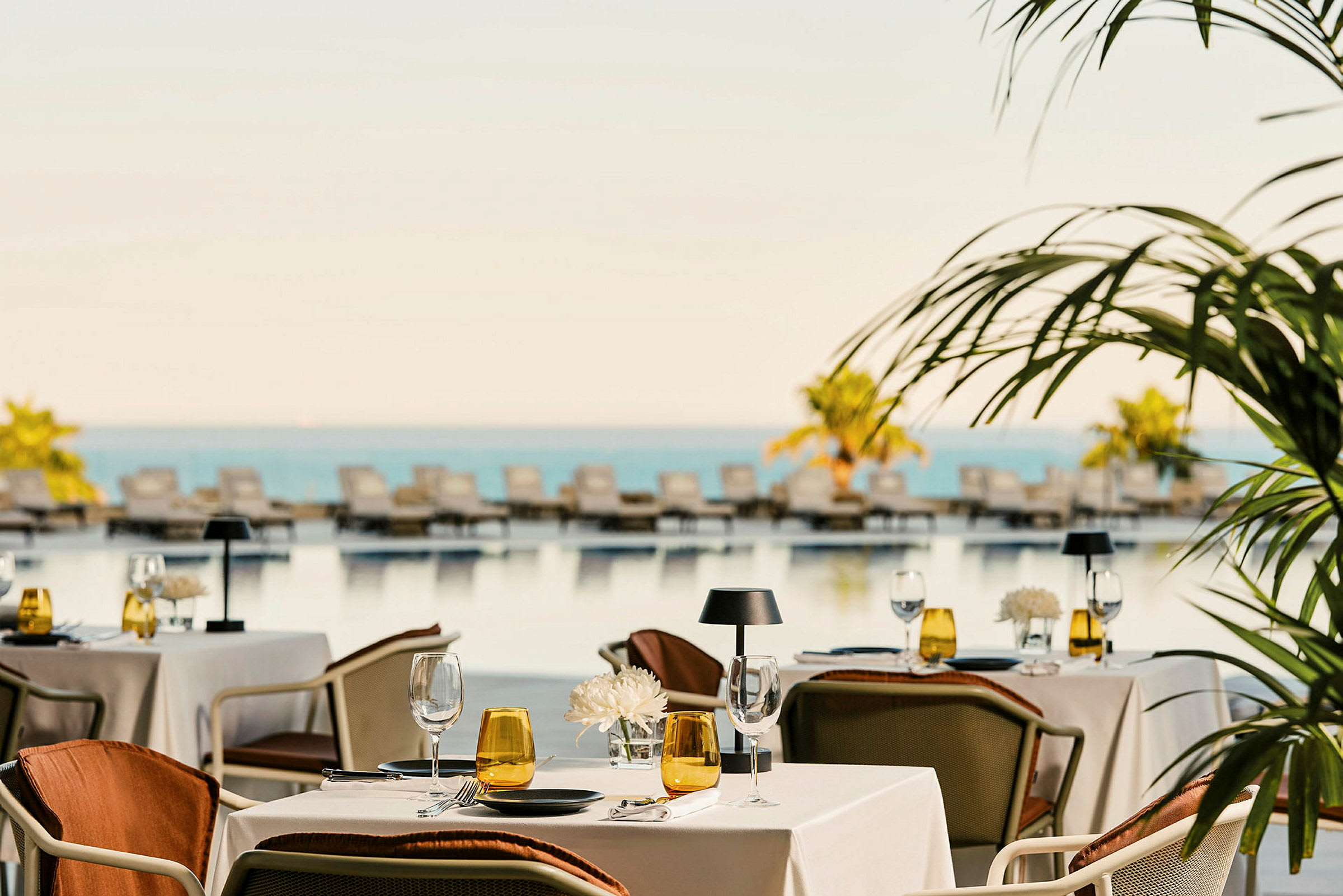 En restaurang med dukade bord vid en pool med solstolar och utsikt över havet. (AI-genererad text)