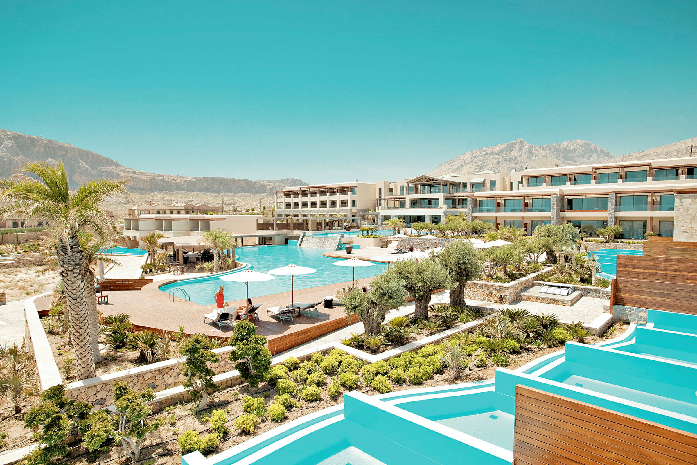 En modern resort med flera byggnader, en stor pool, parasoller och omgivande grönska. (AI-genererad text)