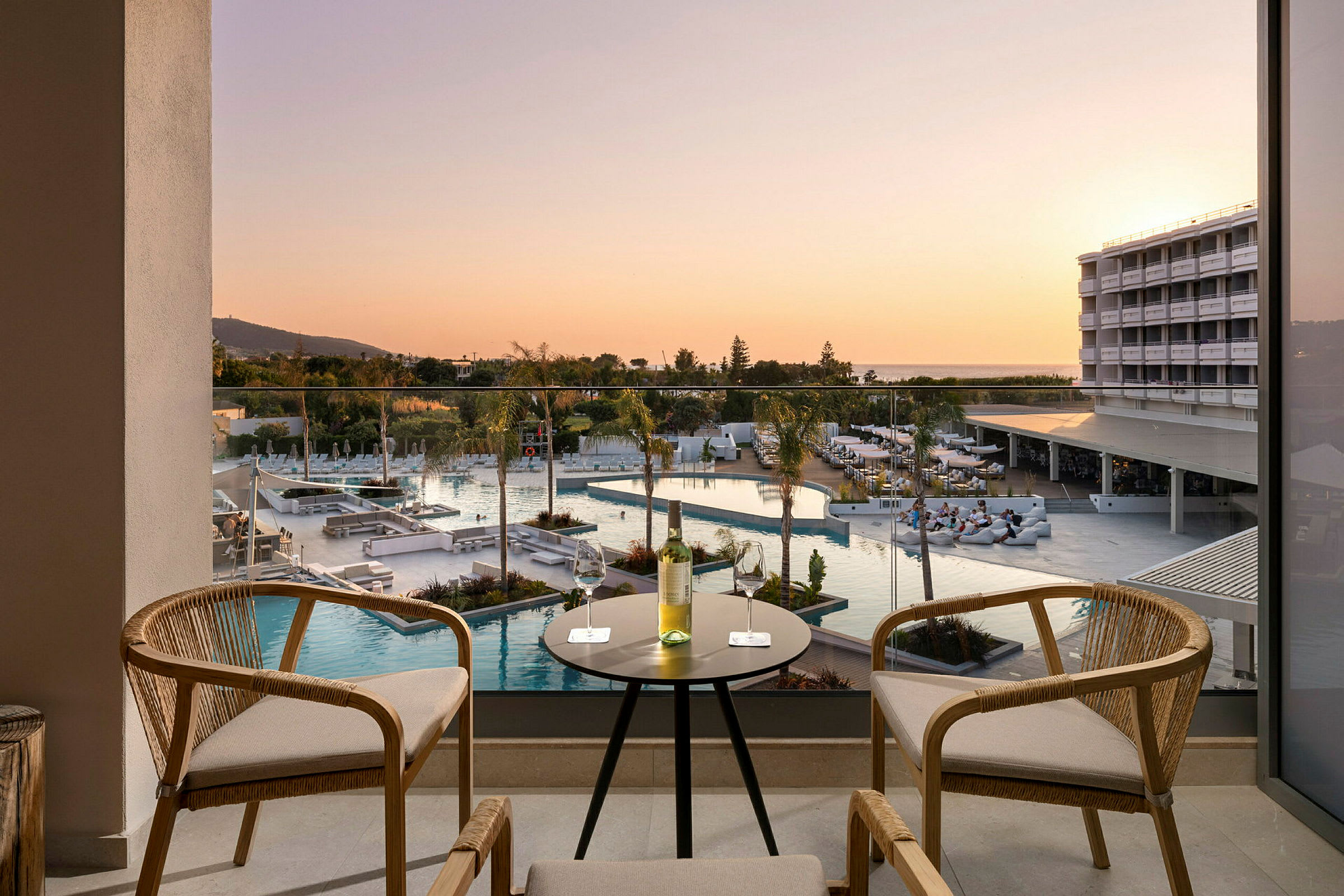 Uteplats med bord och stolar, utsikt över poolområde och hotellbyggnad vid solnedgången. (AI-genererad text)