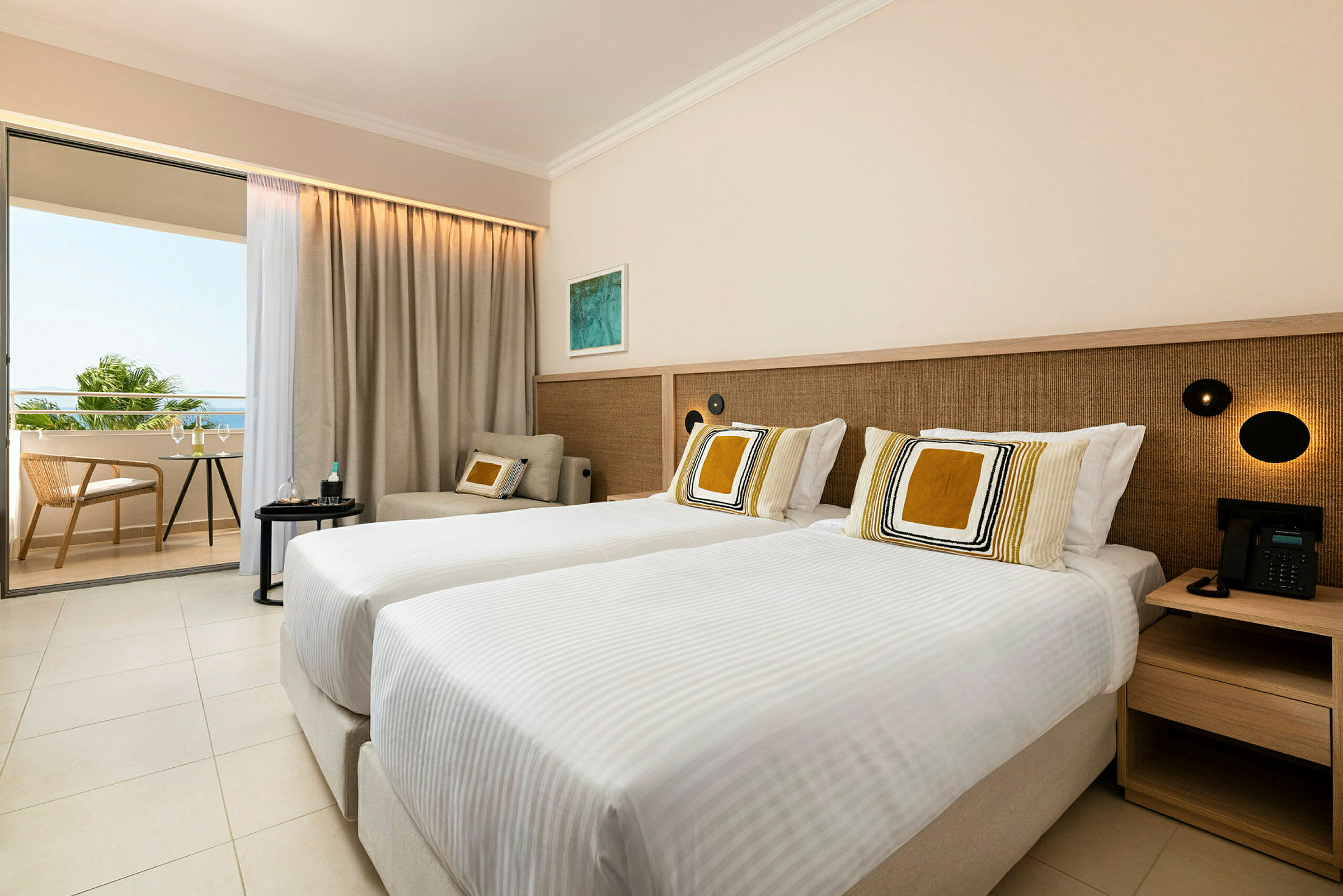 Ett hotellrum med två enkelsängar, en sittgrupp och en balkong som visar utsikt över grönska och himmel. (AI-genererad text)