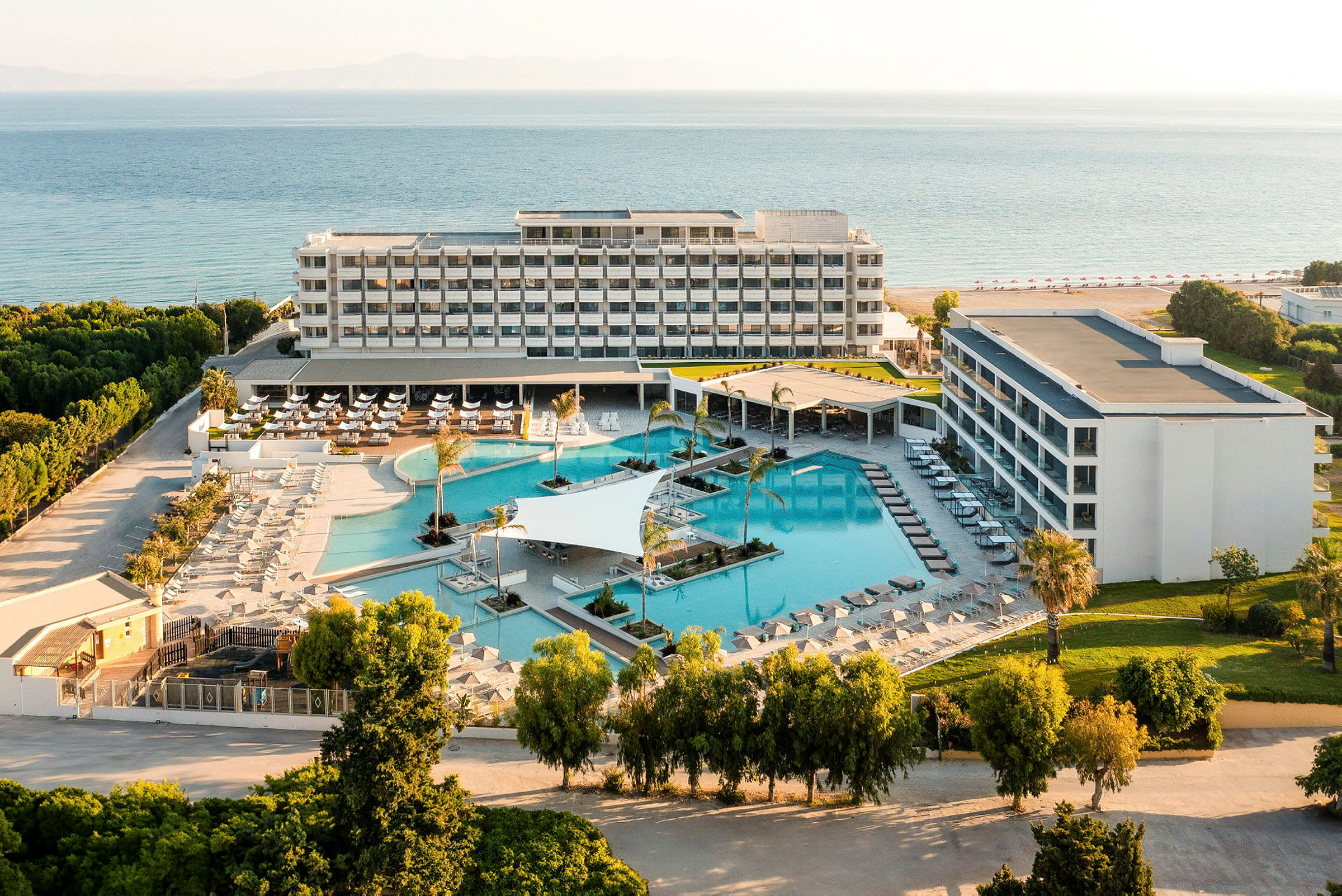 Flygfoto av ett hotellkomplex med poolområde och hav i bakgrunden. (AI-genererad text)