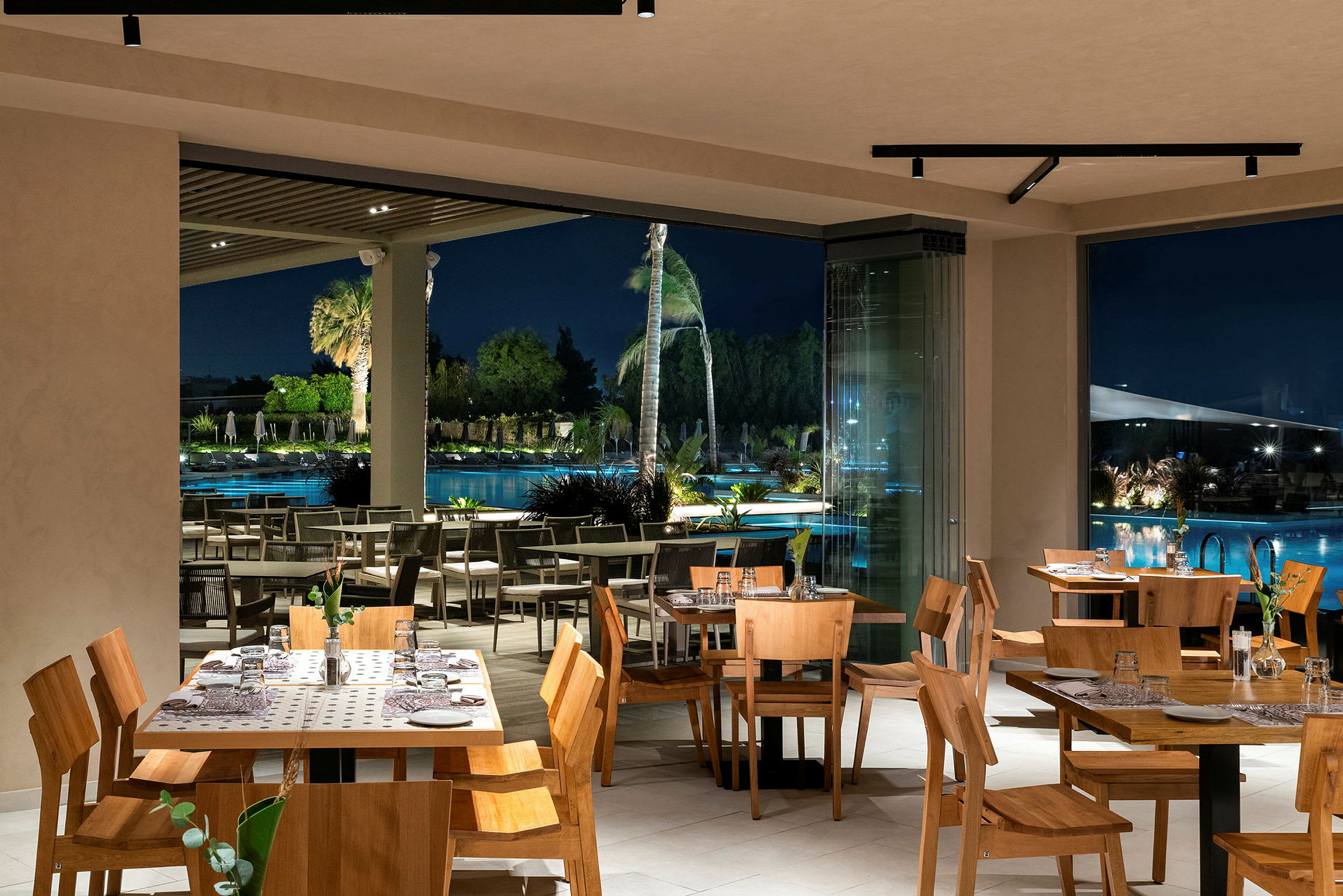 Restaurang interiör med träbord och stolar, utsikt över poolområdet på natten. (AI-genererad text)