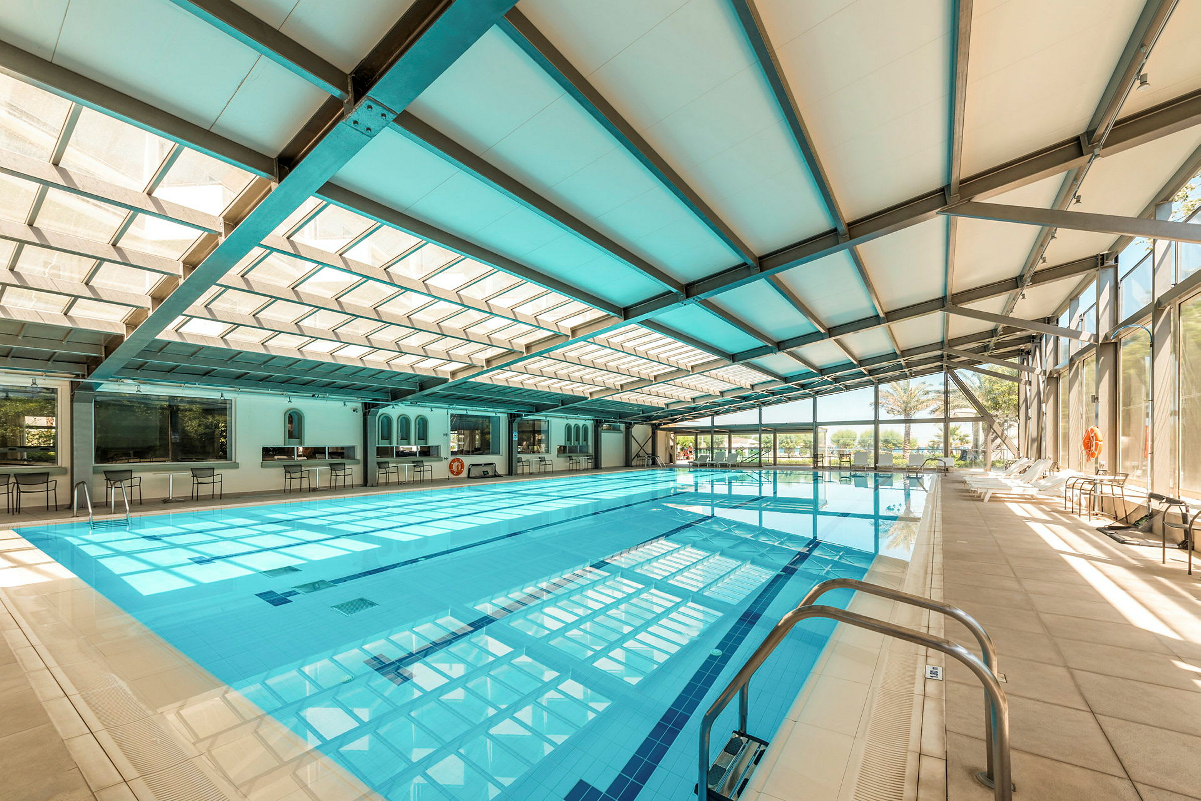 Inomhuspoolområde med en stor pool, stolar längs kanten och glasväggar som släpper in ljus. (AI-genererad text)