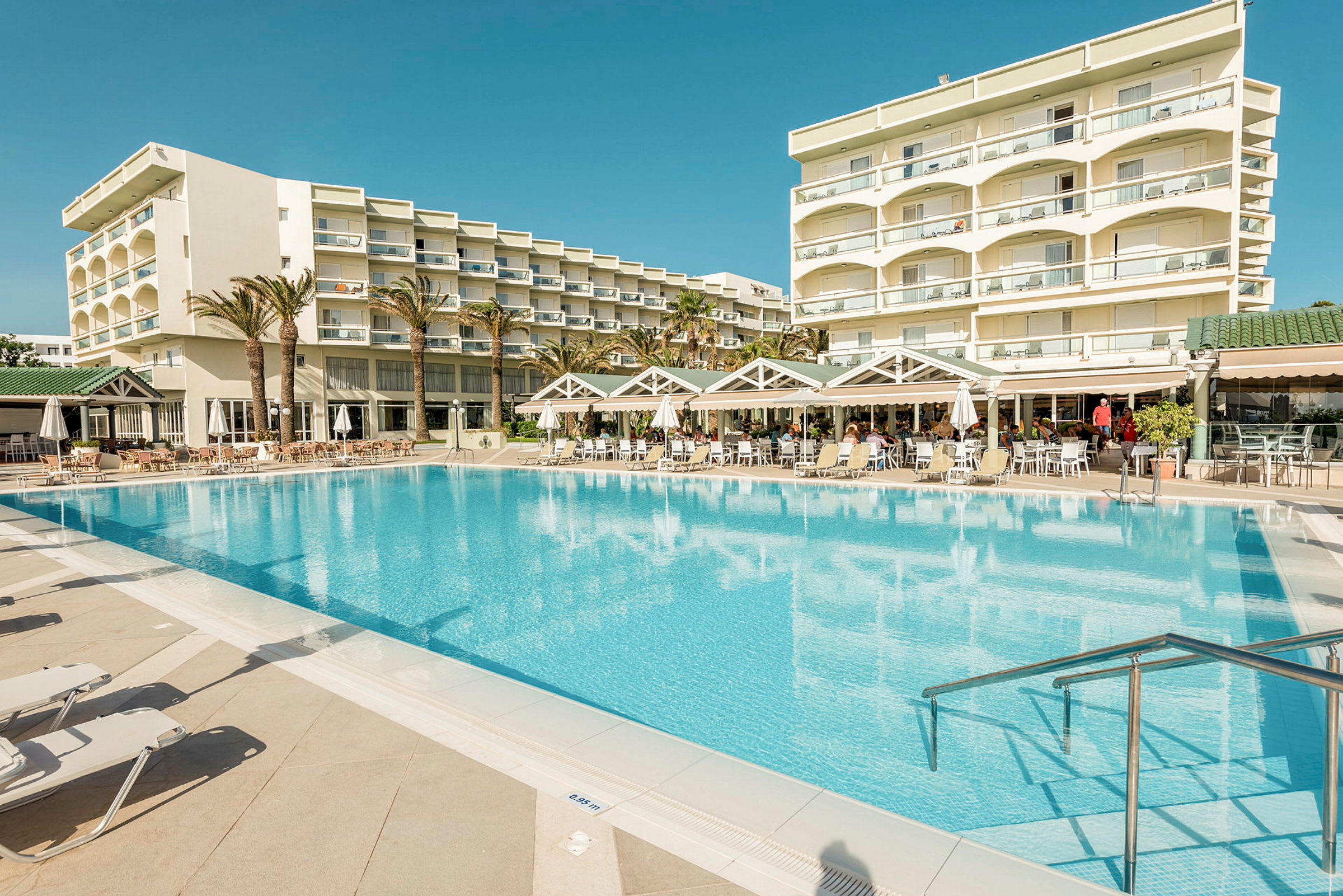 Utomhuspool med solstolar och en hotellbyggnad i bakgrunden. (AI-genererad text)