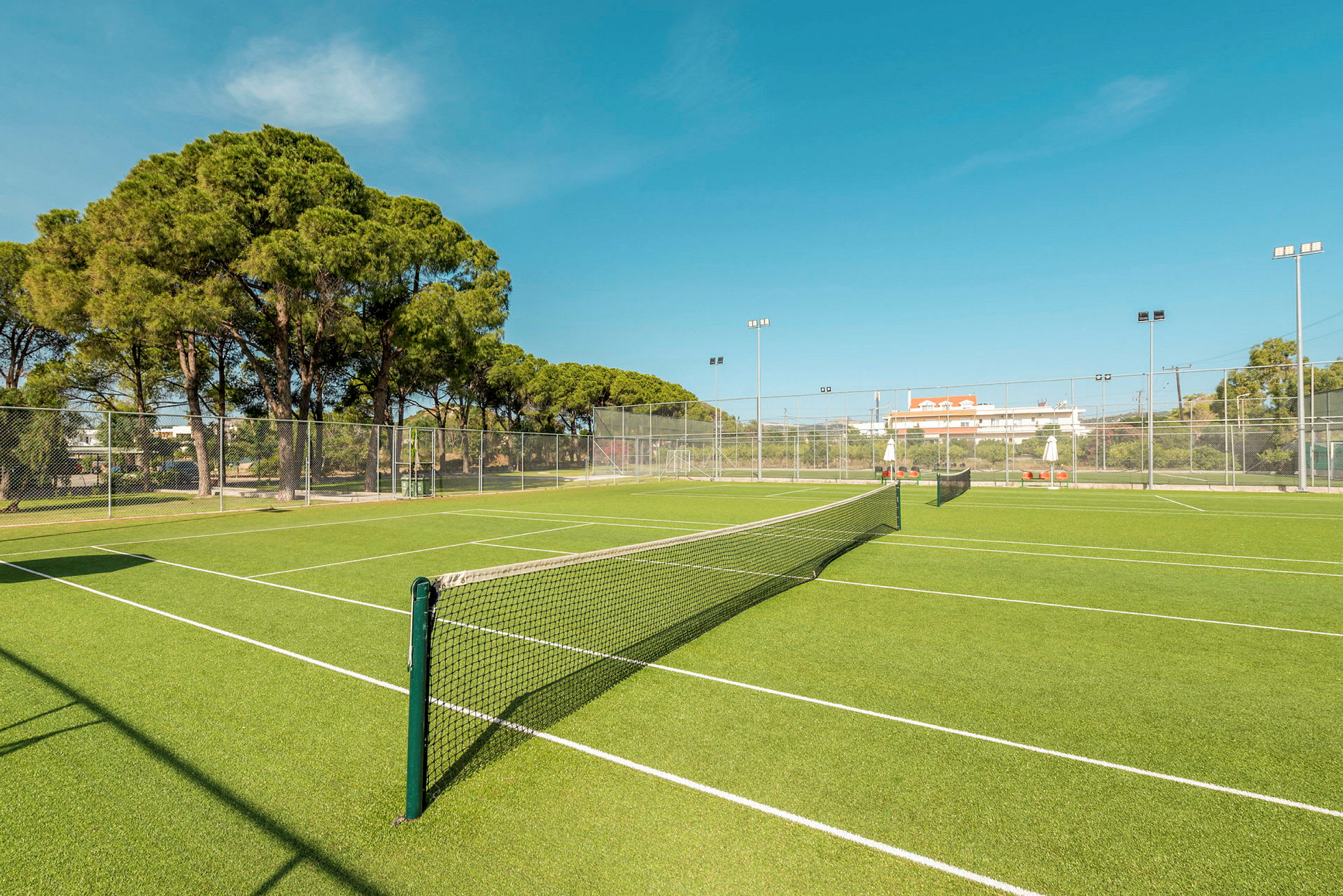 En grön tennisbana med nät och omgivande staket. (AI-genererad text)