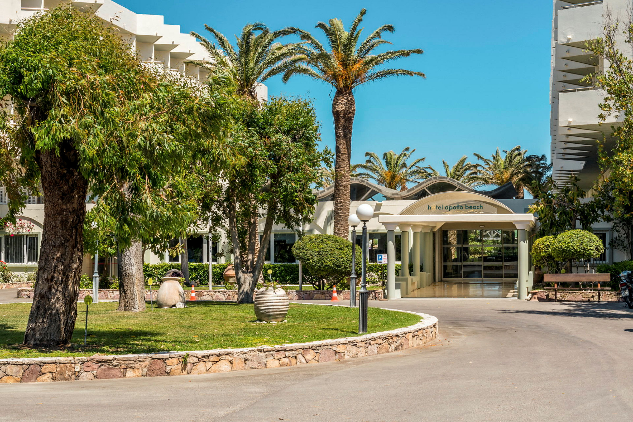Entrén till Hotel Apollo Beach omgiven av palmer och grönska. (AI-genererad text)