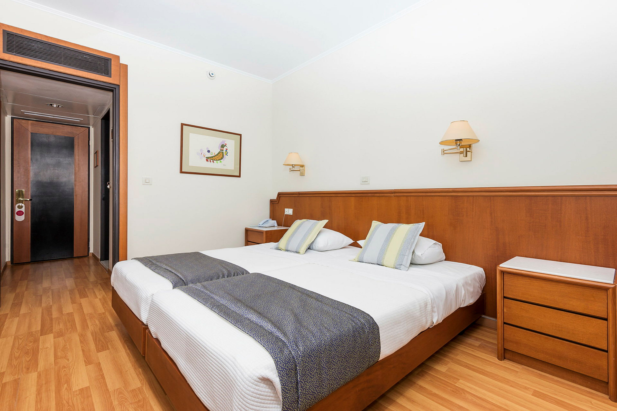 Ett hotellrum med två enkelsängar, trägolv och en dörr i bakgrunden. (AI-genererad text)