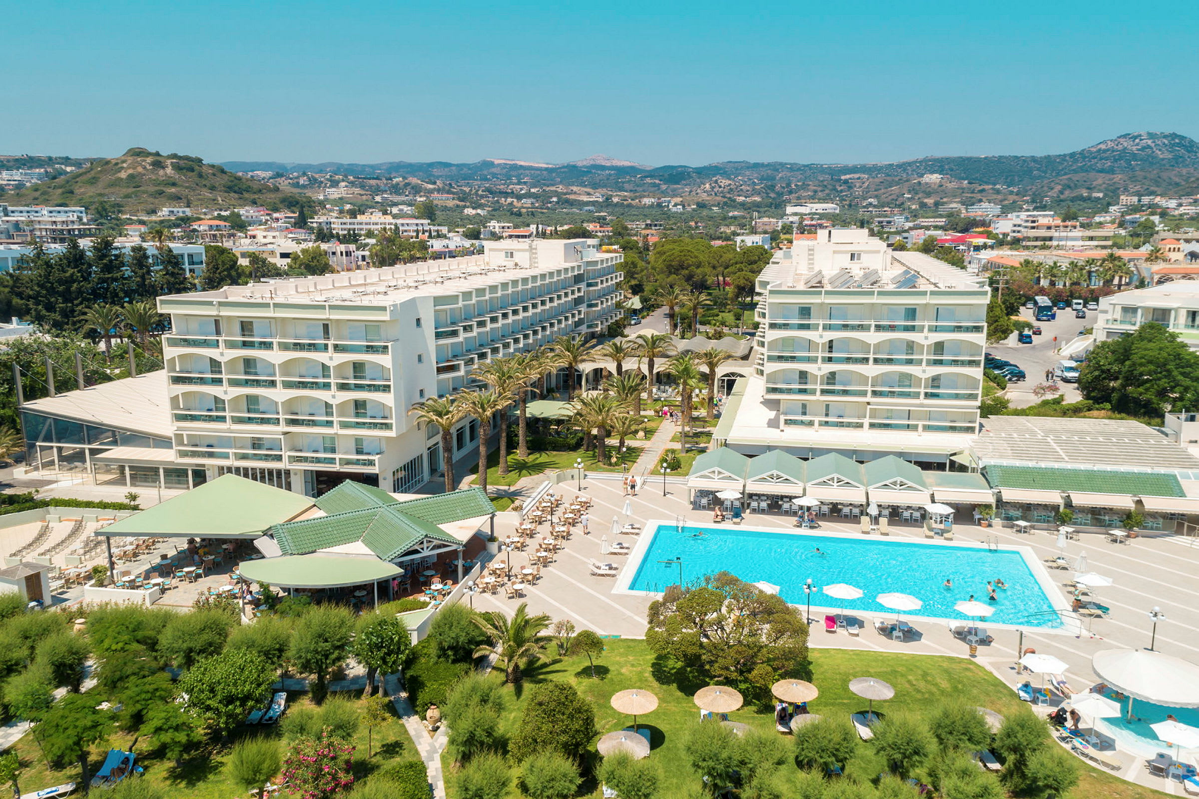 Flygfoto av ett hotellområde med pool, grönskande trädgård och byggnader. (AI-genererad text)