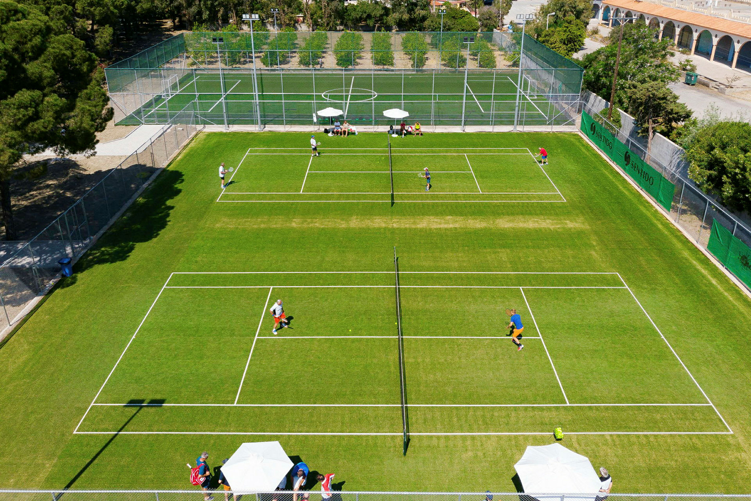 Flygbild av en tennisbana med spelare och omgivande träd. (AI-genererad text)