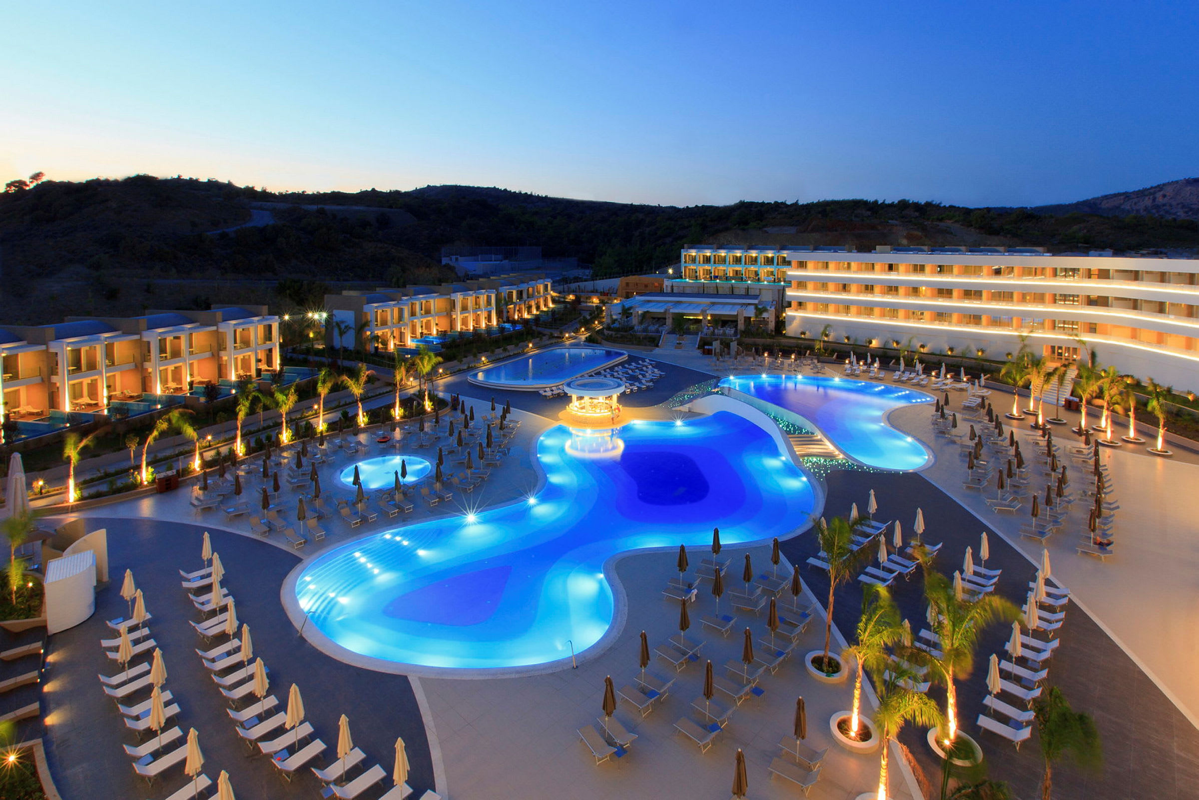 Hotellets nattbelysning vid poolområdet med solstolar och omgivande byggnader. (AI-genererad text)