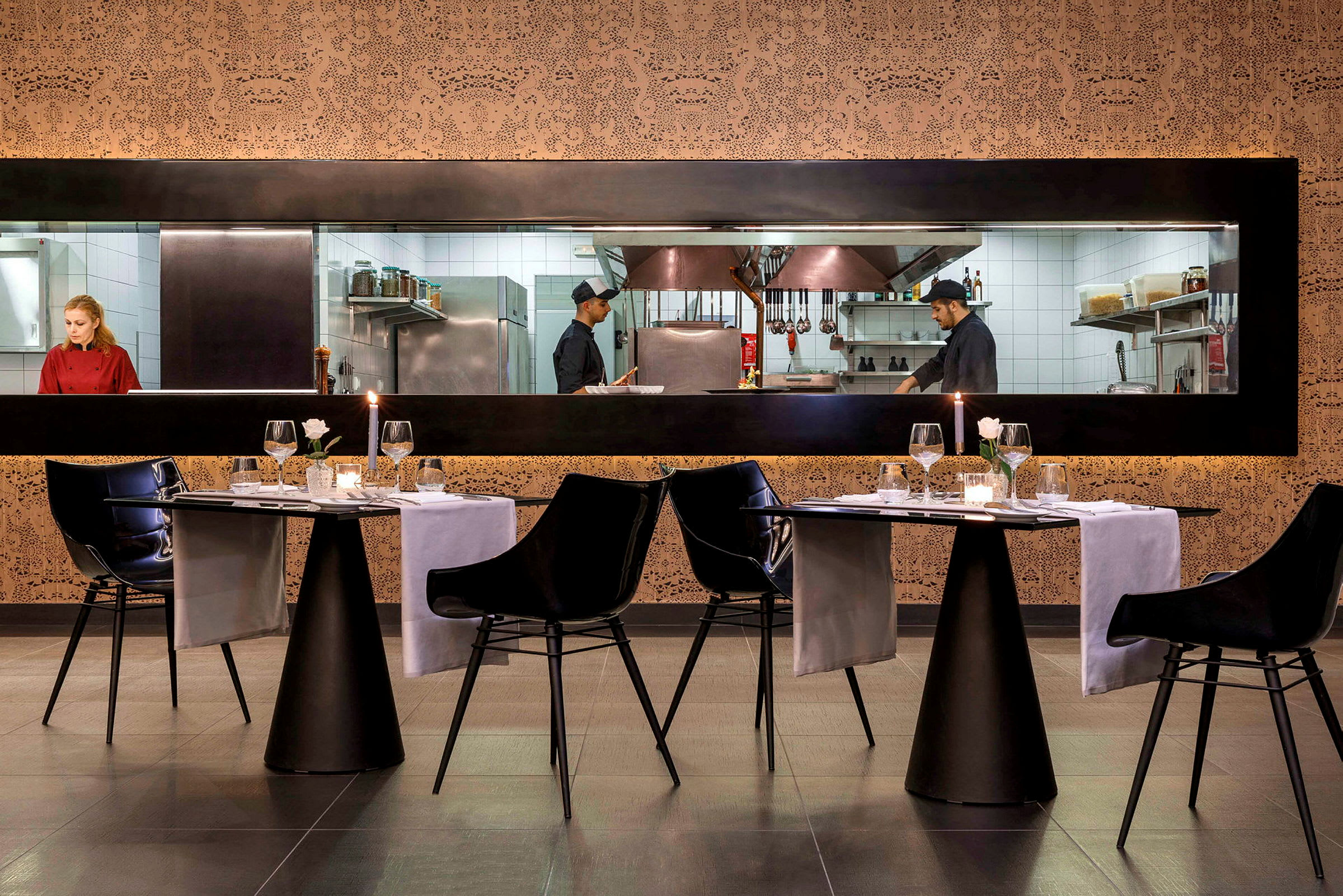 Bild på en restaurang med upplysta bordsarrangemang och synligt kök genom en glasruta. (AI-genererad text)
