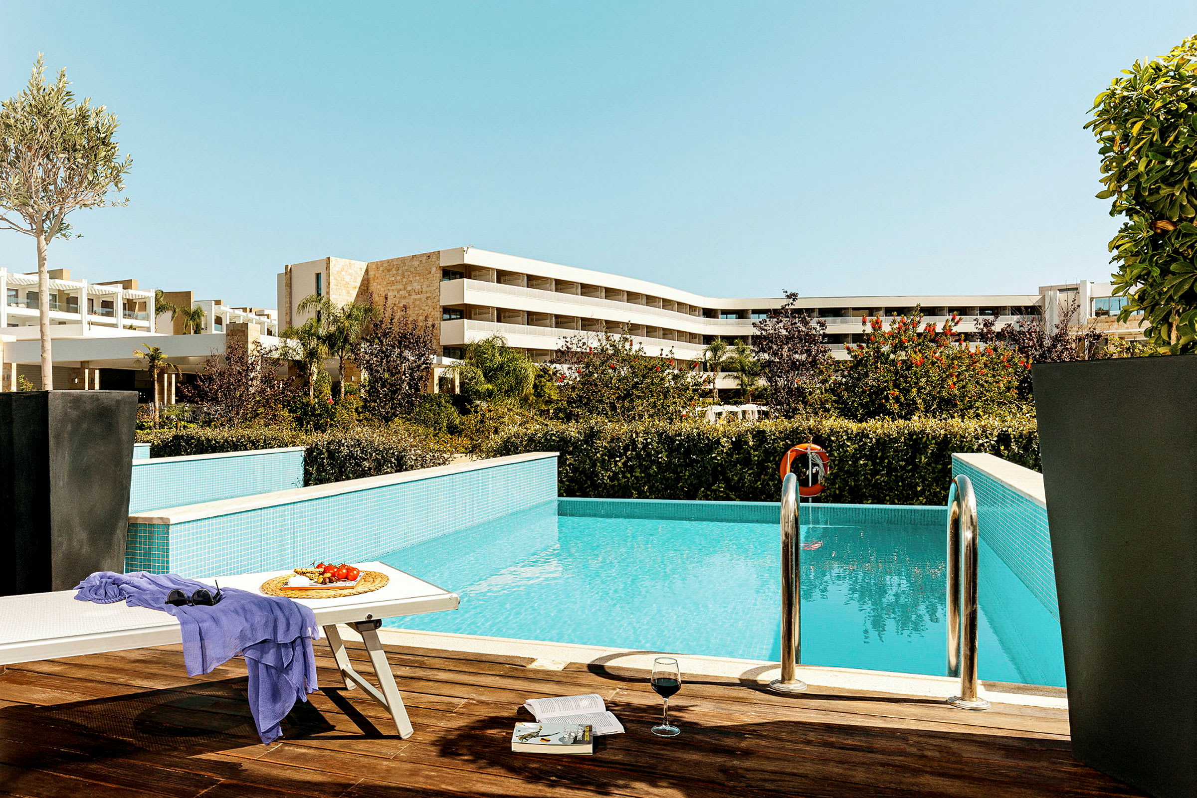 Utomhusområde med pool, solstol, bord med frukt och glas samt hotellbyggnader i bakgrunden. (AI-genererad text)